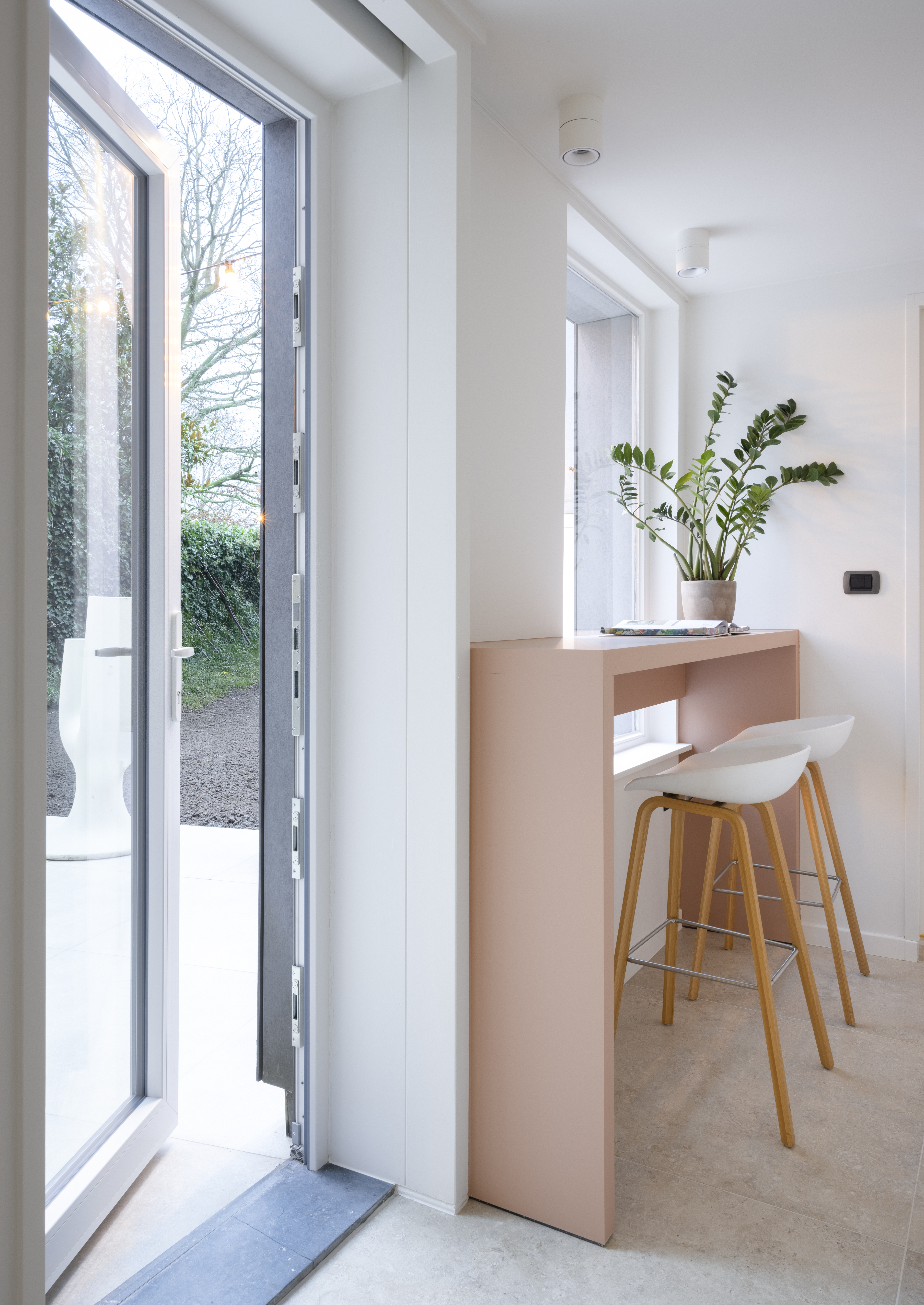 Witte beglaasde PVC-deur uit IMPAKT PLUS in een modern gerenoveerde gesloten bebouwing, geopend naast een lichte keuken met bar, barkrukken en plant.