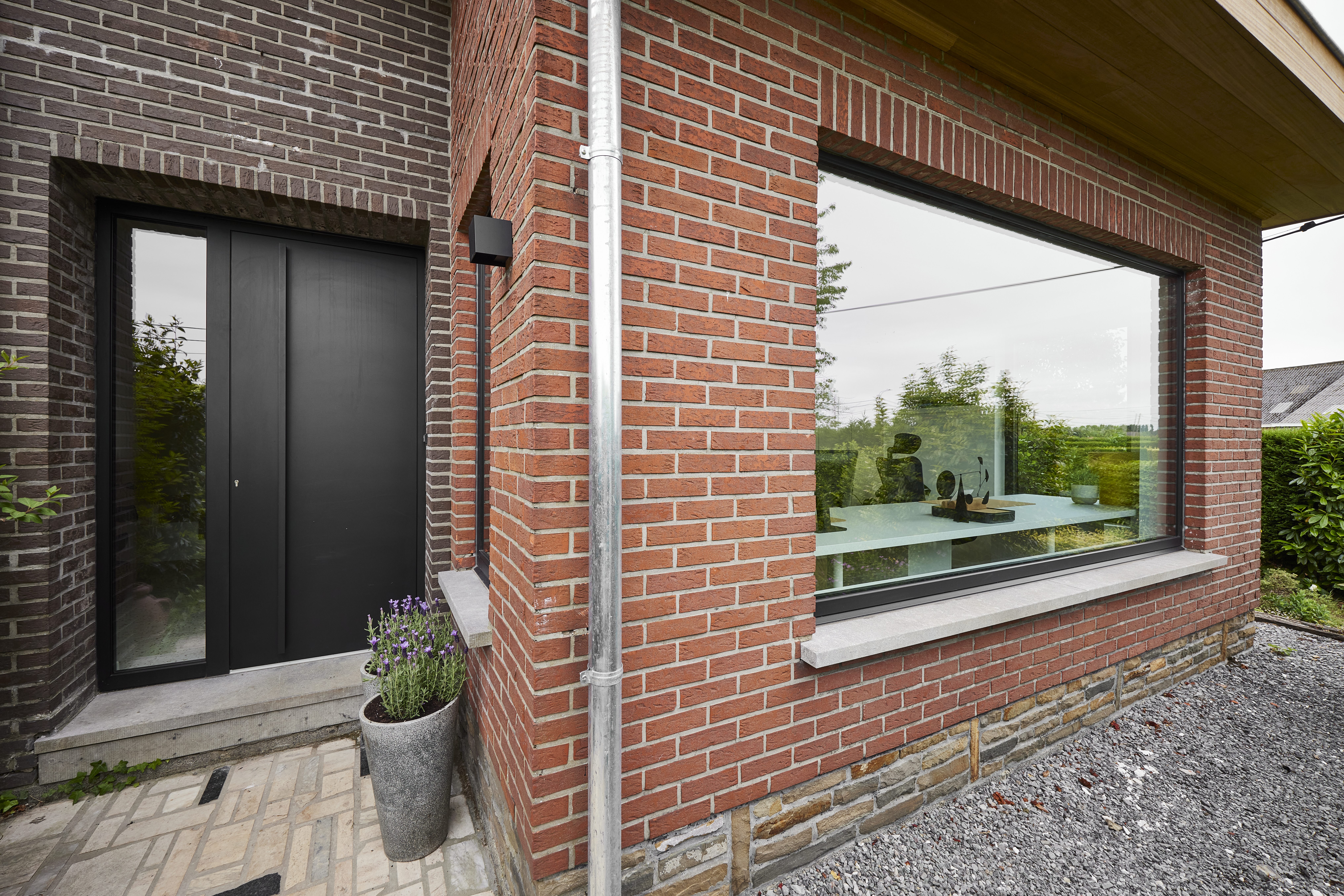 Grafietzwart aluminium vast raam naast een zwarte deur met zijlicht en paneel, geïntegreerd in een moderne bakstenen gevel.