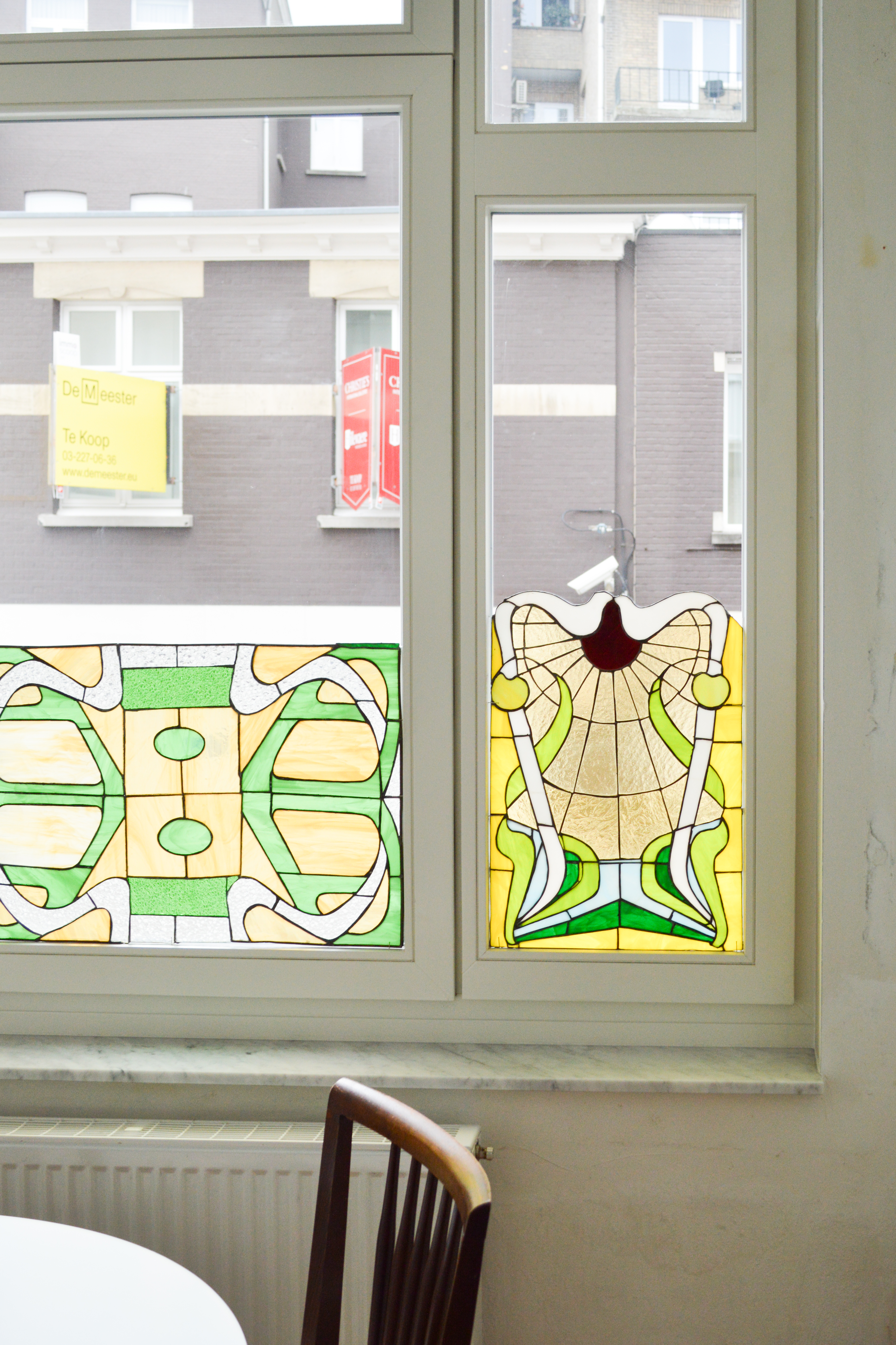 Gerenoveerd raam in verfijnde klassieke stijl, met vast raam, draai-kipgedeelte, bovenlicht, afgelakte raamprofielen en kleurrijke glas-in-loodpanelen.