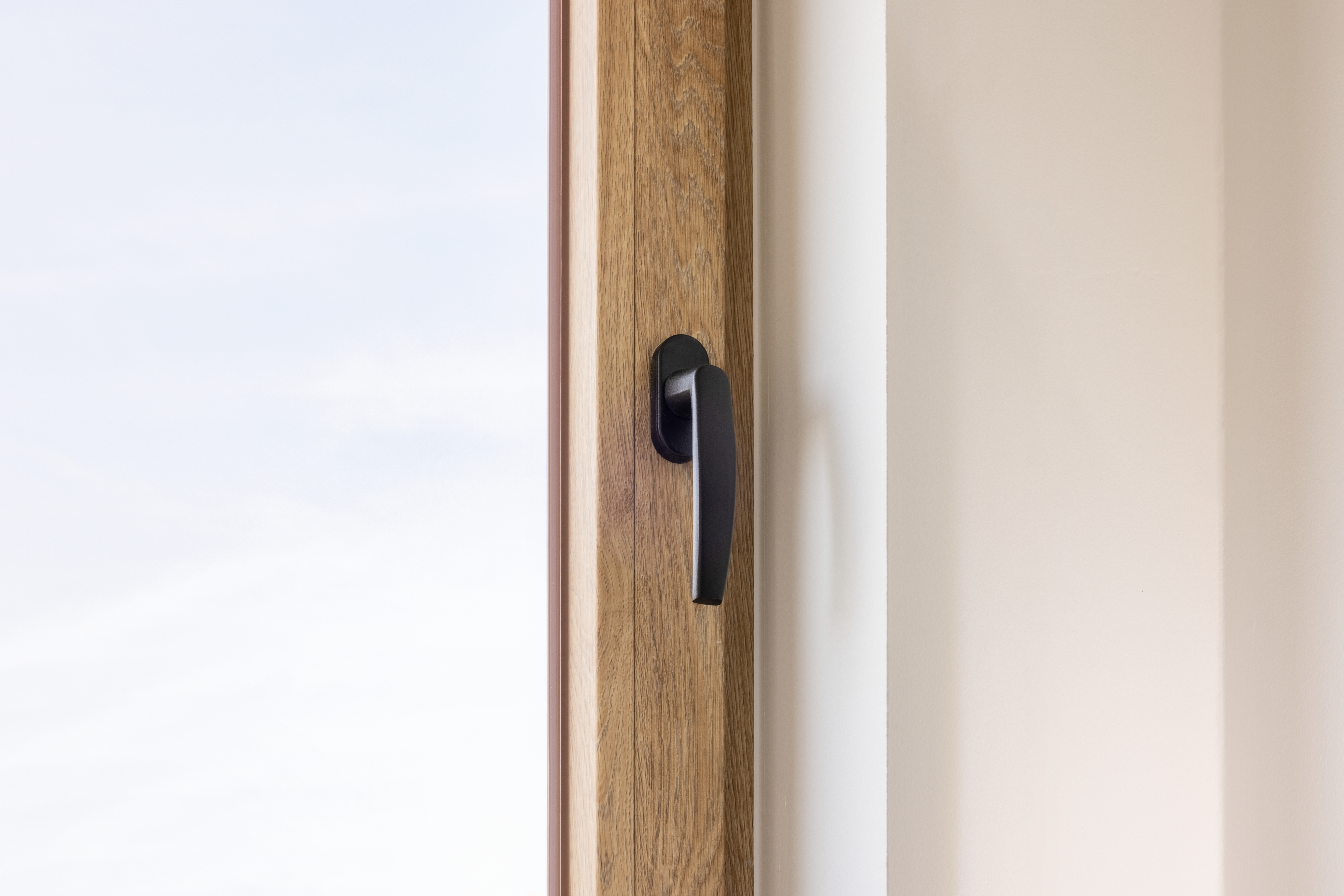 Detail van een gesloten draai-kipraam met natuurlijk eiklook, zichtbare houtnerf en zwarte raamgreep in een tijdloos gerenoveerd interieur.