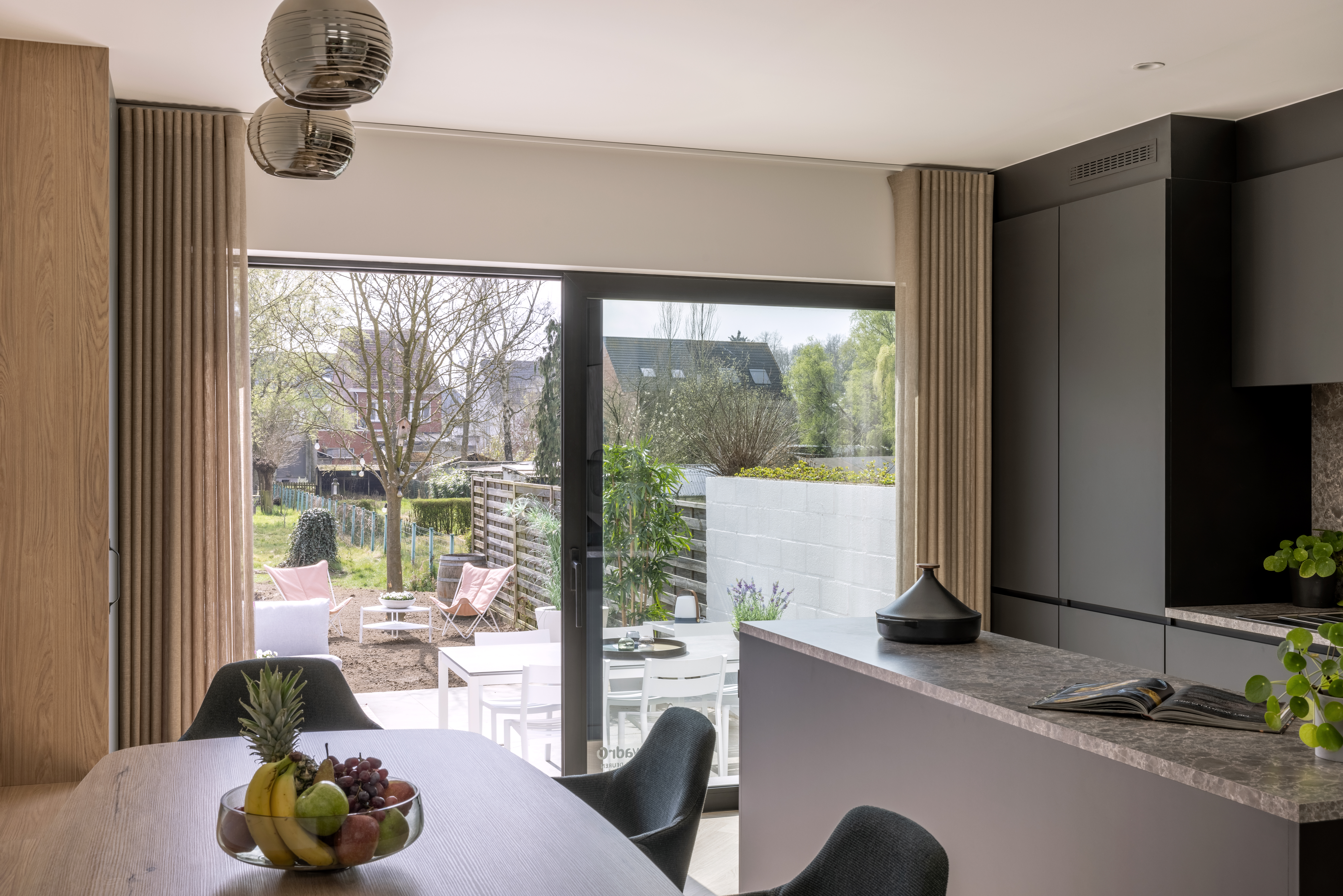 Modern interieur met een grafietzwart ALU Visoglide Monorail-schuifraam, dat uitkijkt op een terras en groene tuin.