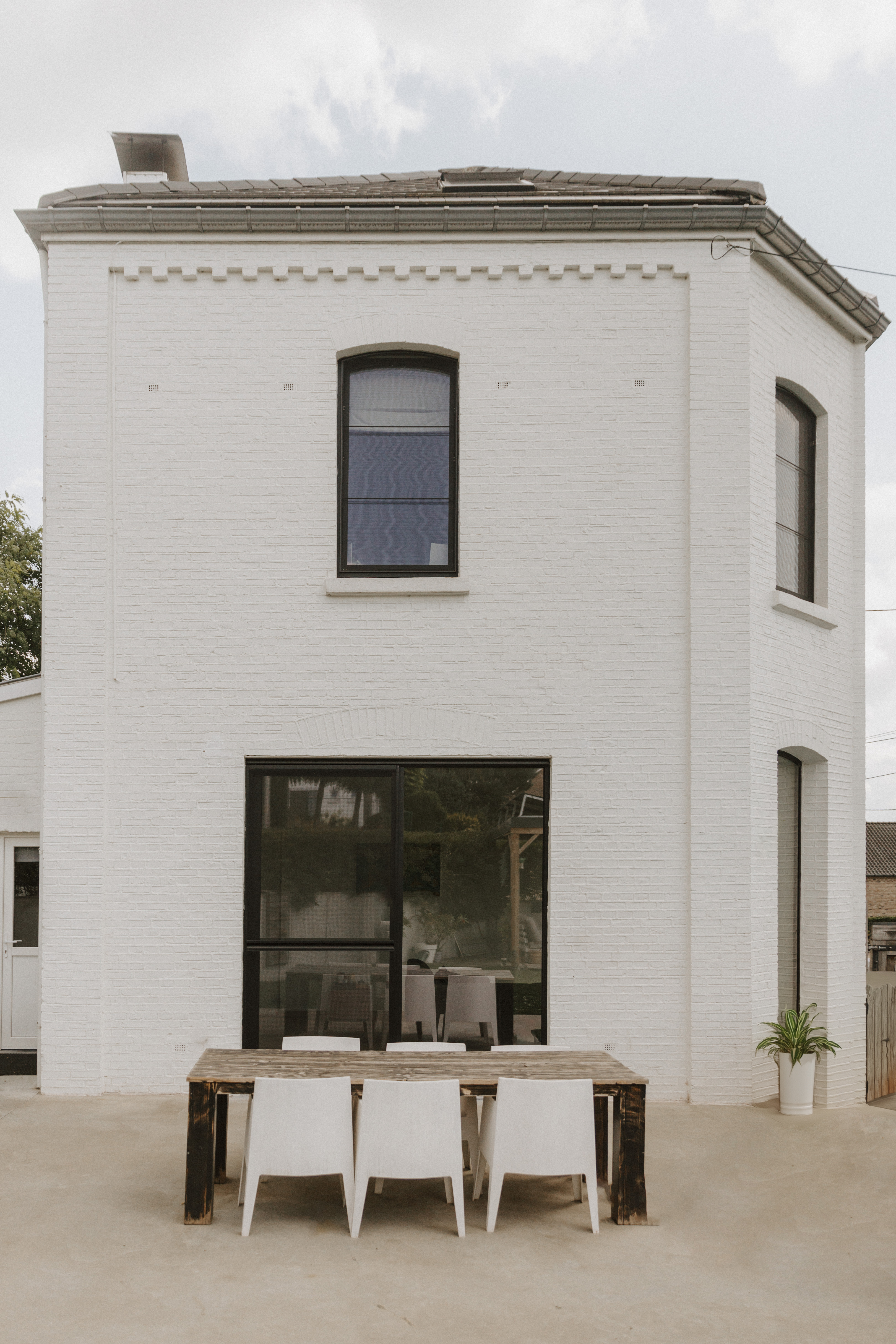 Wit gebouw met diepzwarte aluminiumramen: een draai-kipraam op de verdieping en een groot schuifraam naast het terras.
