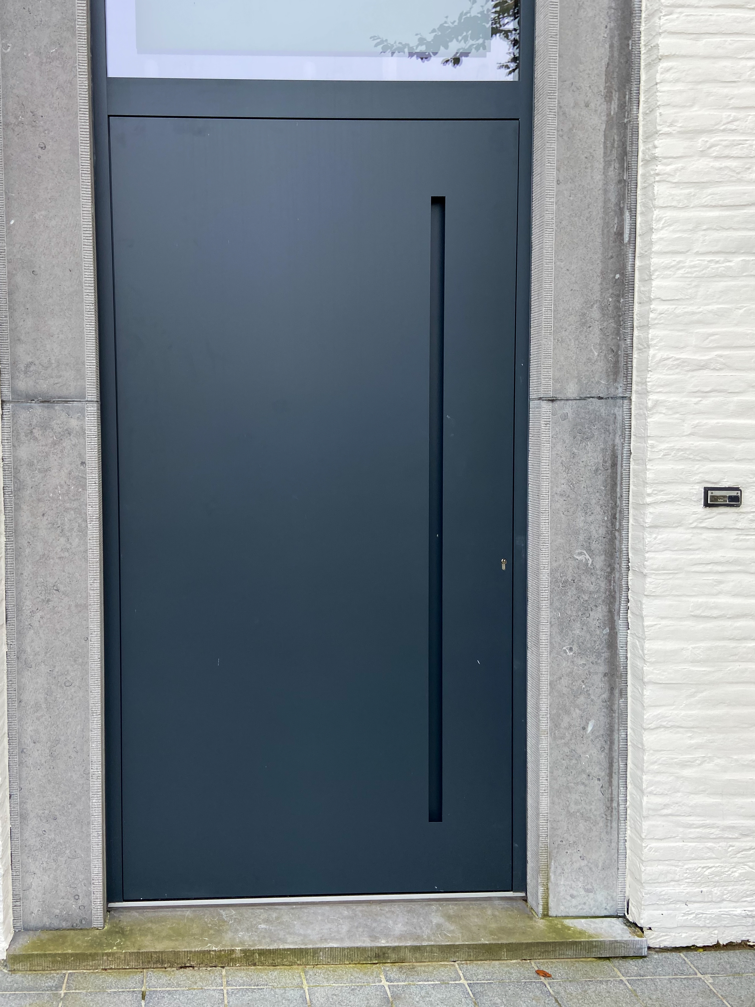 Anthracietkleurige voordeur met smal beglaasd bovenlicht in de gerenoveerde gevel van een vrijstaande woning.