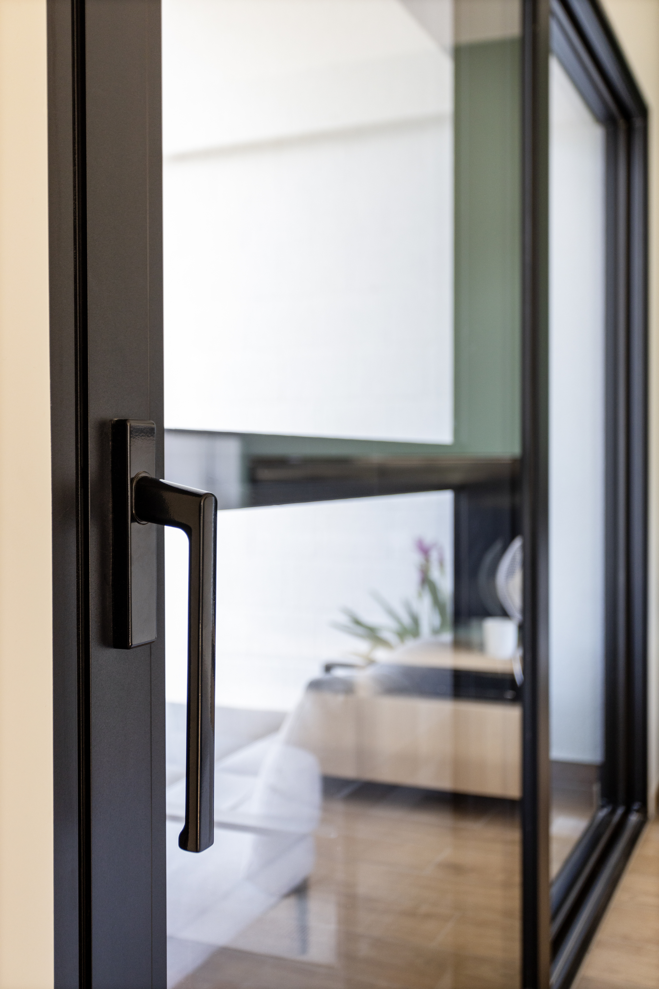 Modern zwart mat aluminium schuifraam met lange handgreep in een gerenoveerde woning met lichte woonkamer en houten vloer.