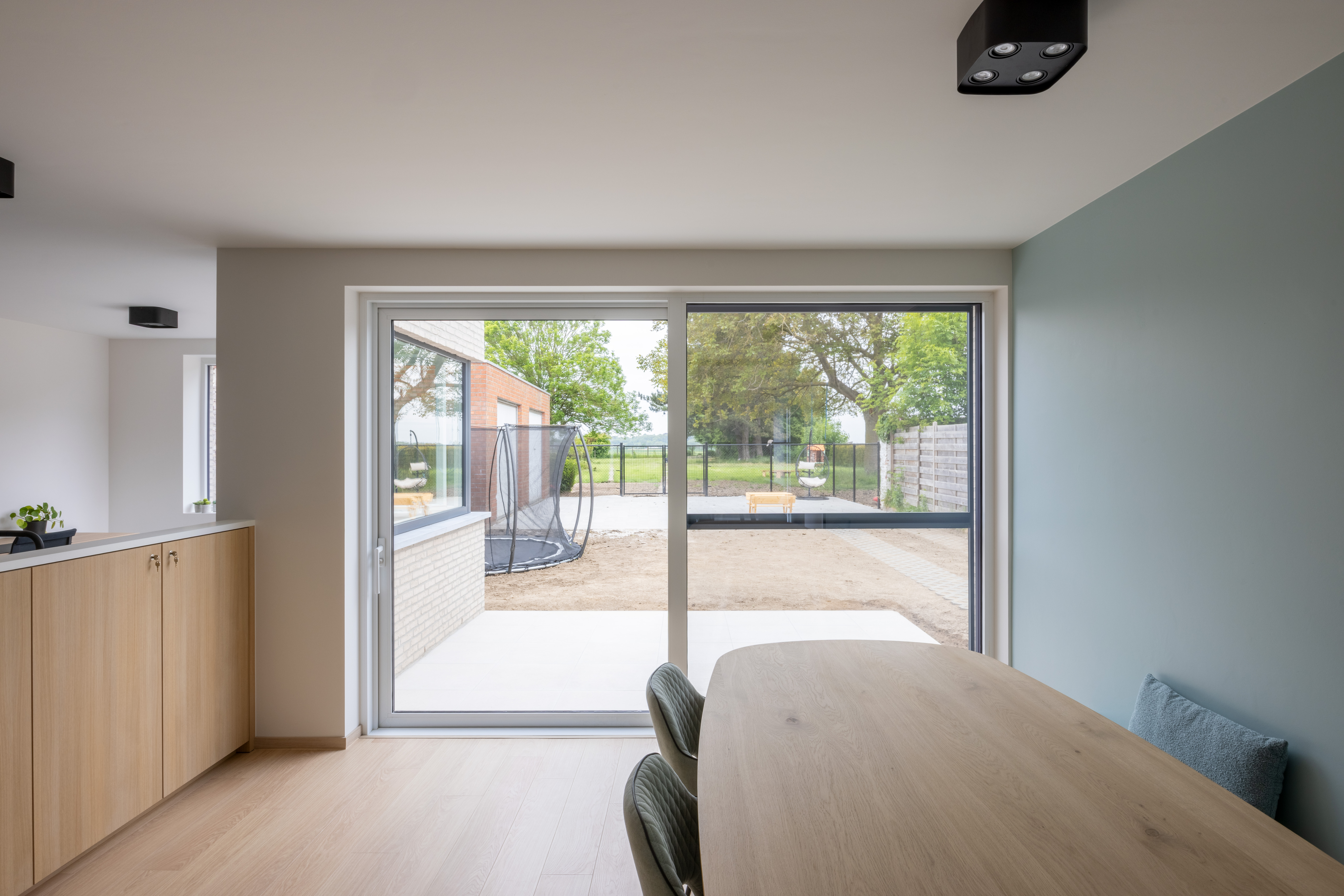 Modern interieur met een matwit aluminium schuifraam en schuifvliegenraam naar een omheinde buitenruimte in een gerenoveerde gesloten woning.