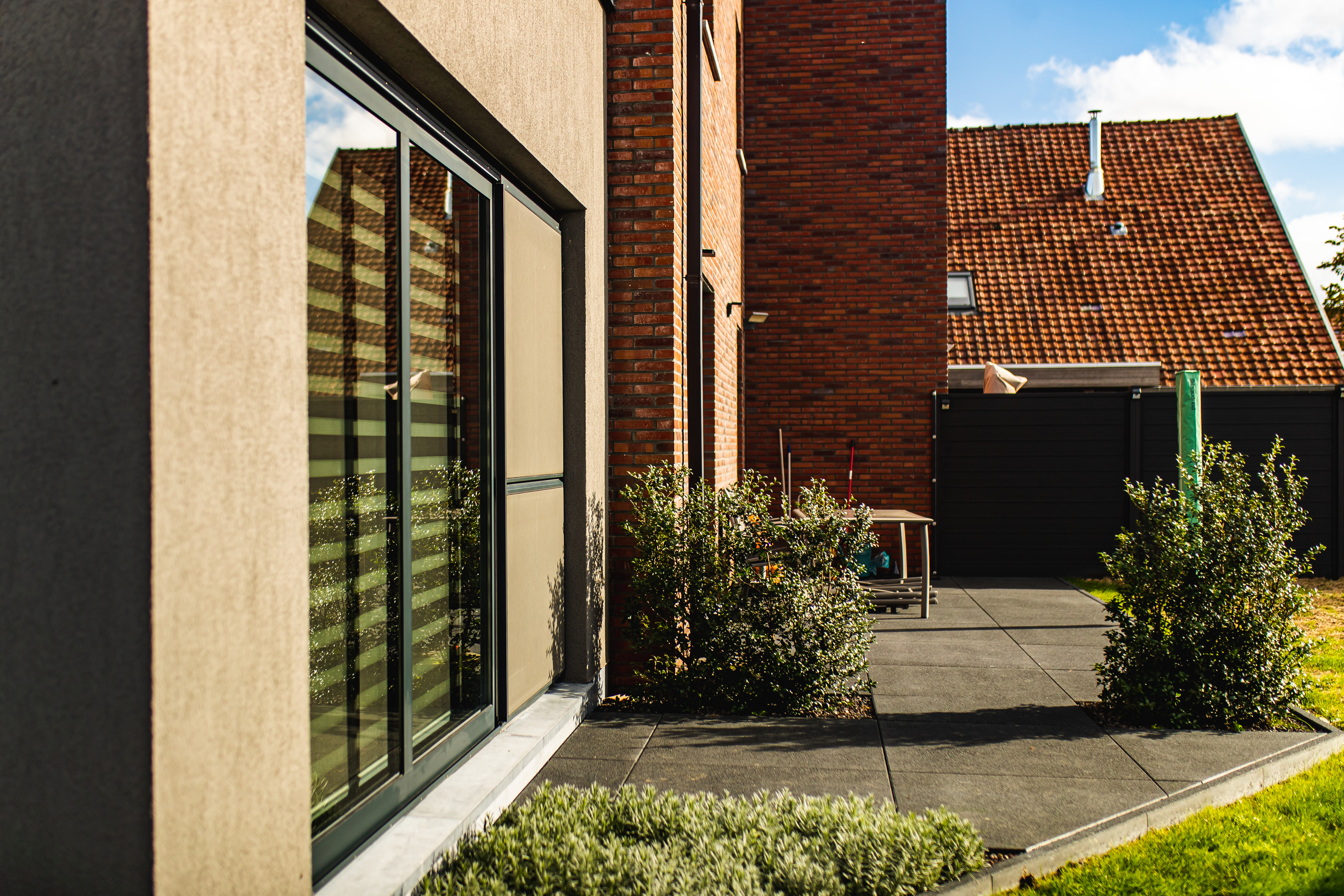 Anthracietgrijs schuifraam in de gevel van een nieuwbouwwoning in open bebouwing, met uitzicht op een betegeld terras.