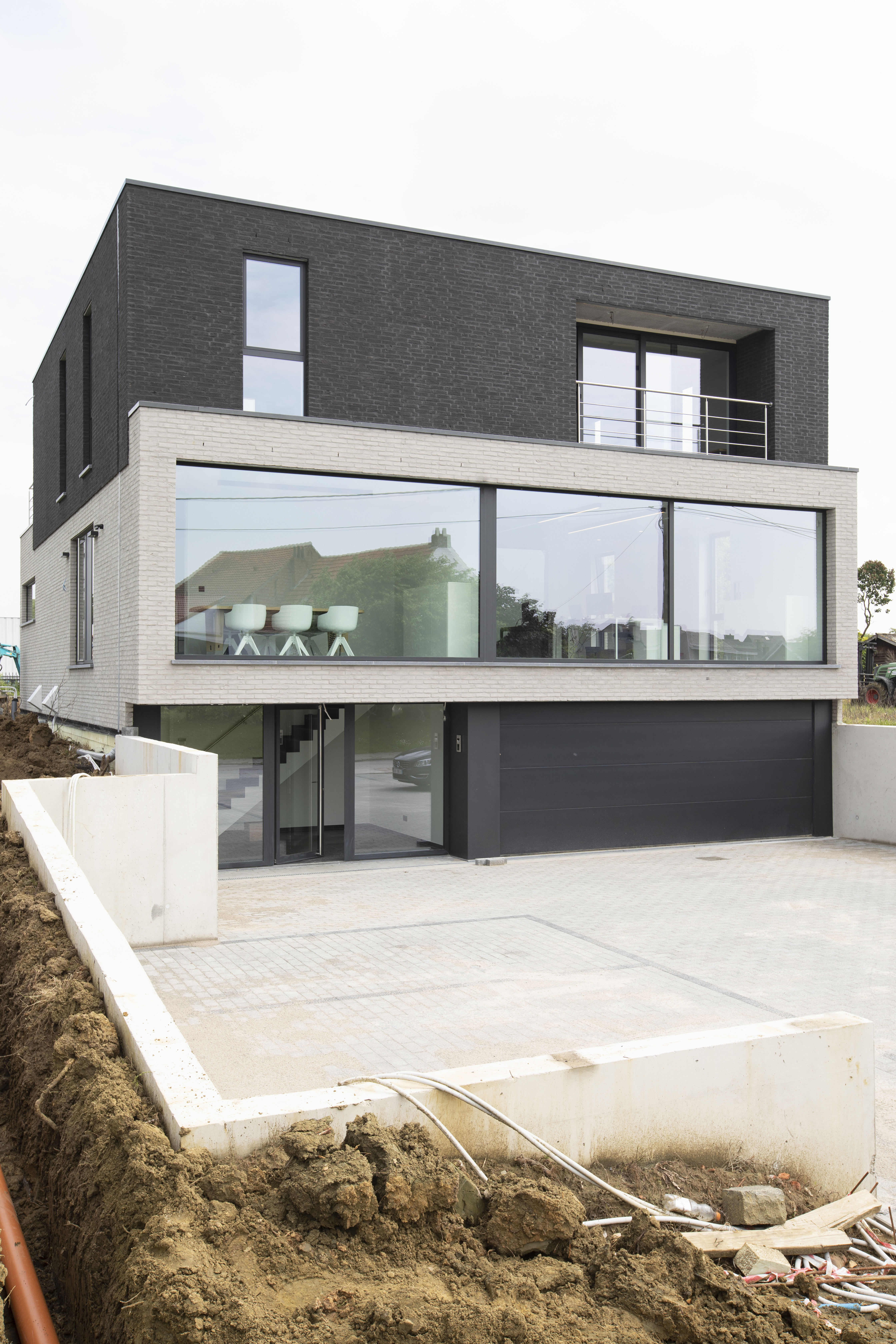 Moderne nieuwbouwwoning in open bebouwing met donkere gevel, grote glaspartijen, overdekte inkom en lichte oprit.