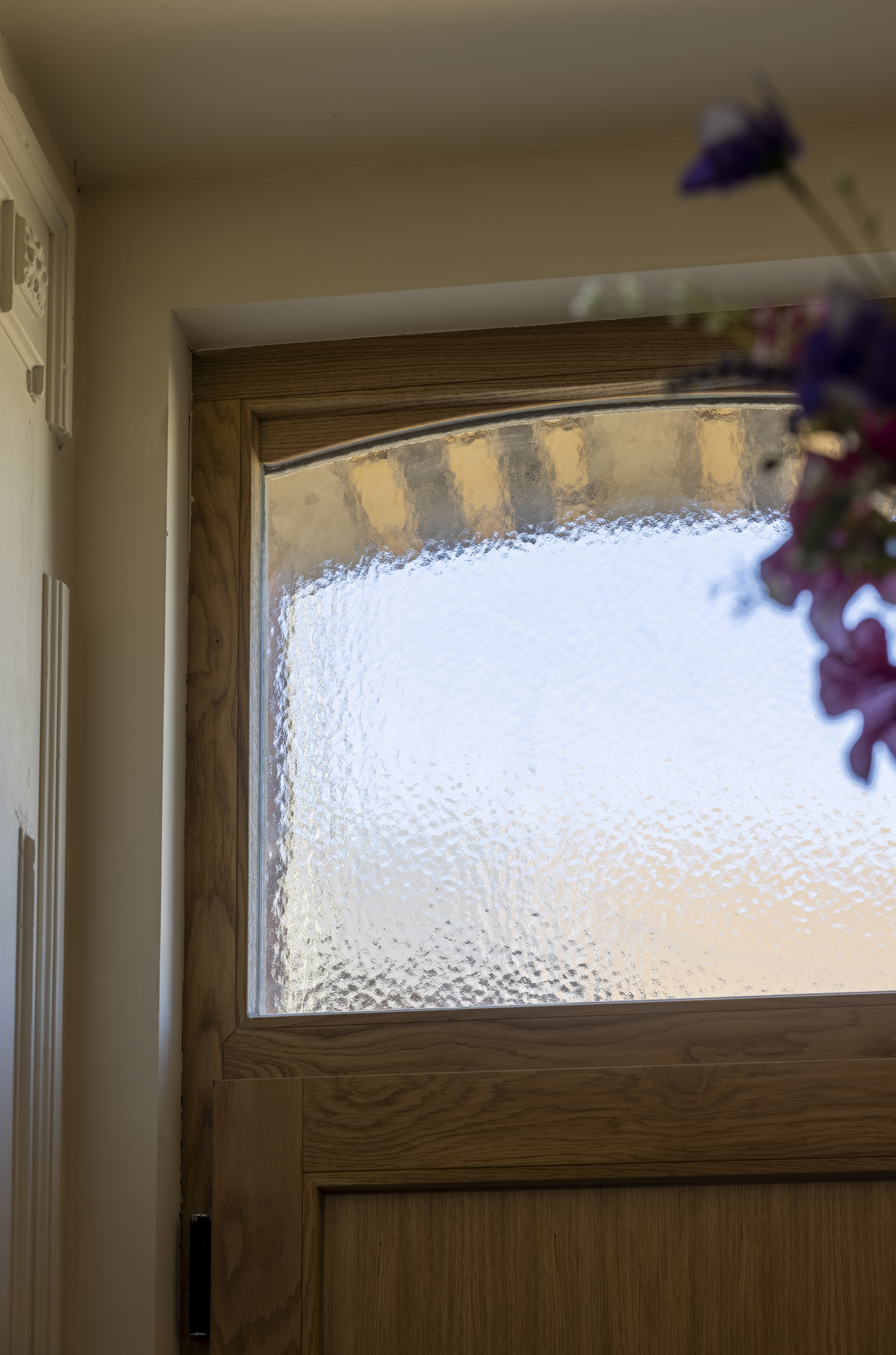 Een eikenhouten deur met bovenlicht en structuurglas bevindt zich in een lichte binnenruimte naast een witte muur.