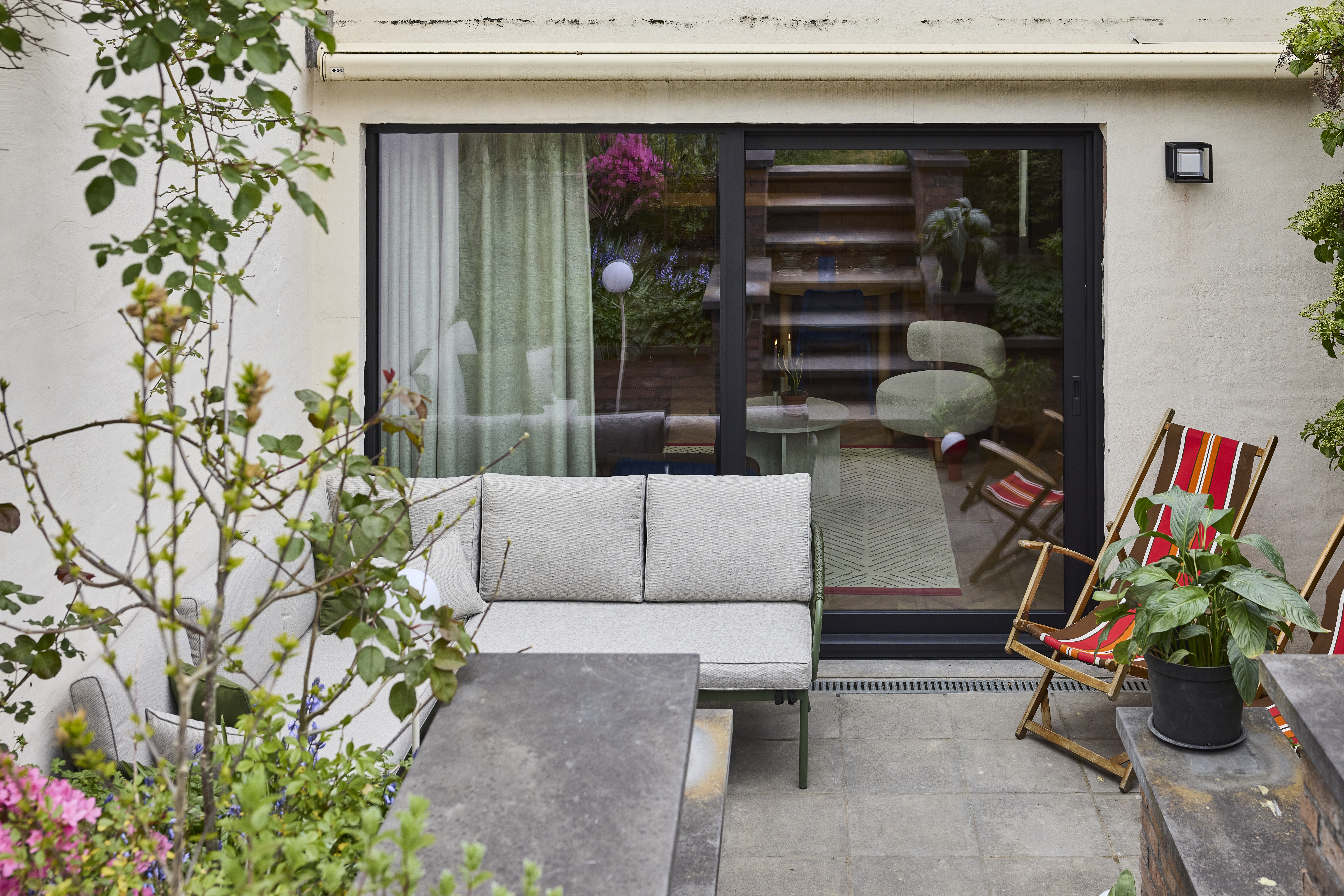 Zwart aluminium schuifraam ALU Visoglide Monorail in een lichte gevel, met zicht op de woonkamer en een ingericht terras met planten.