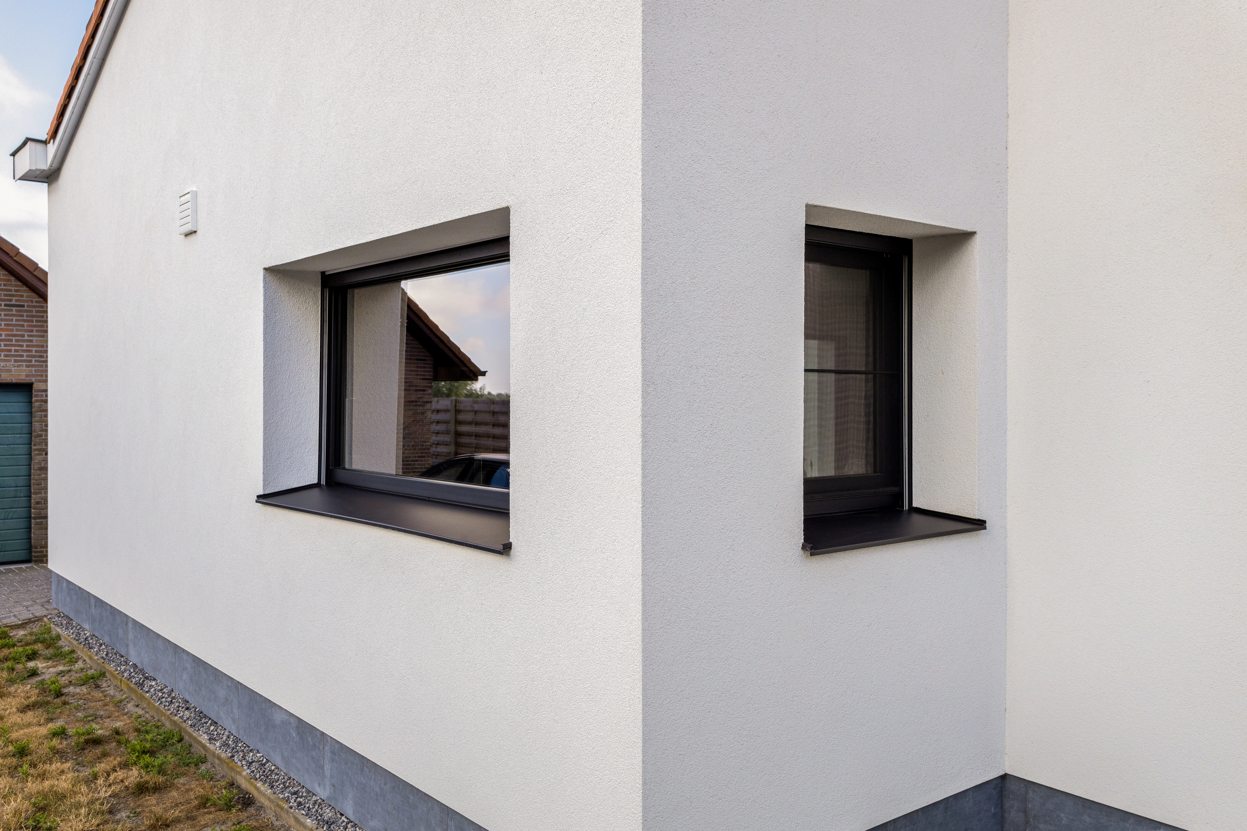 Twee matzwarte ramen in de lichte gevel van een modern gerenoveerde halfopen woning.
