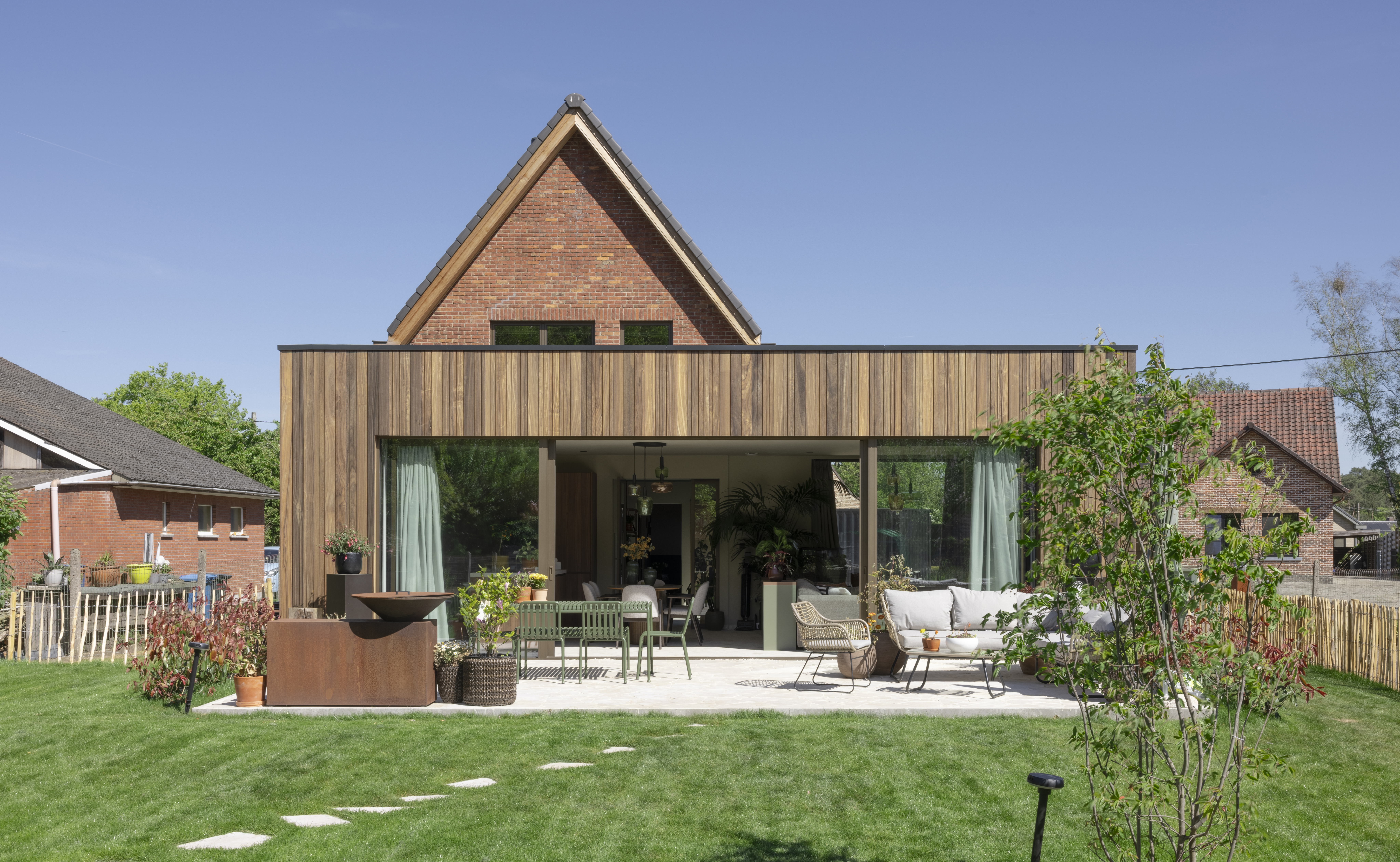 Moderne houten aanbouw aan een bakstenen woning, met een breed ALU Visoglide Monorail-schuifraam in brons geanodiseerde aluminiumprofielen en een terras.