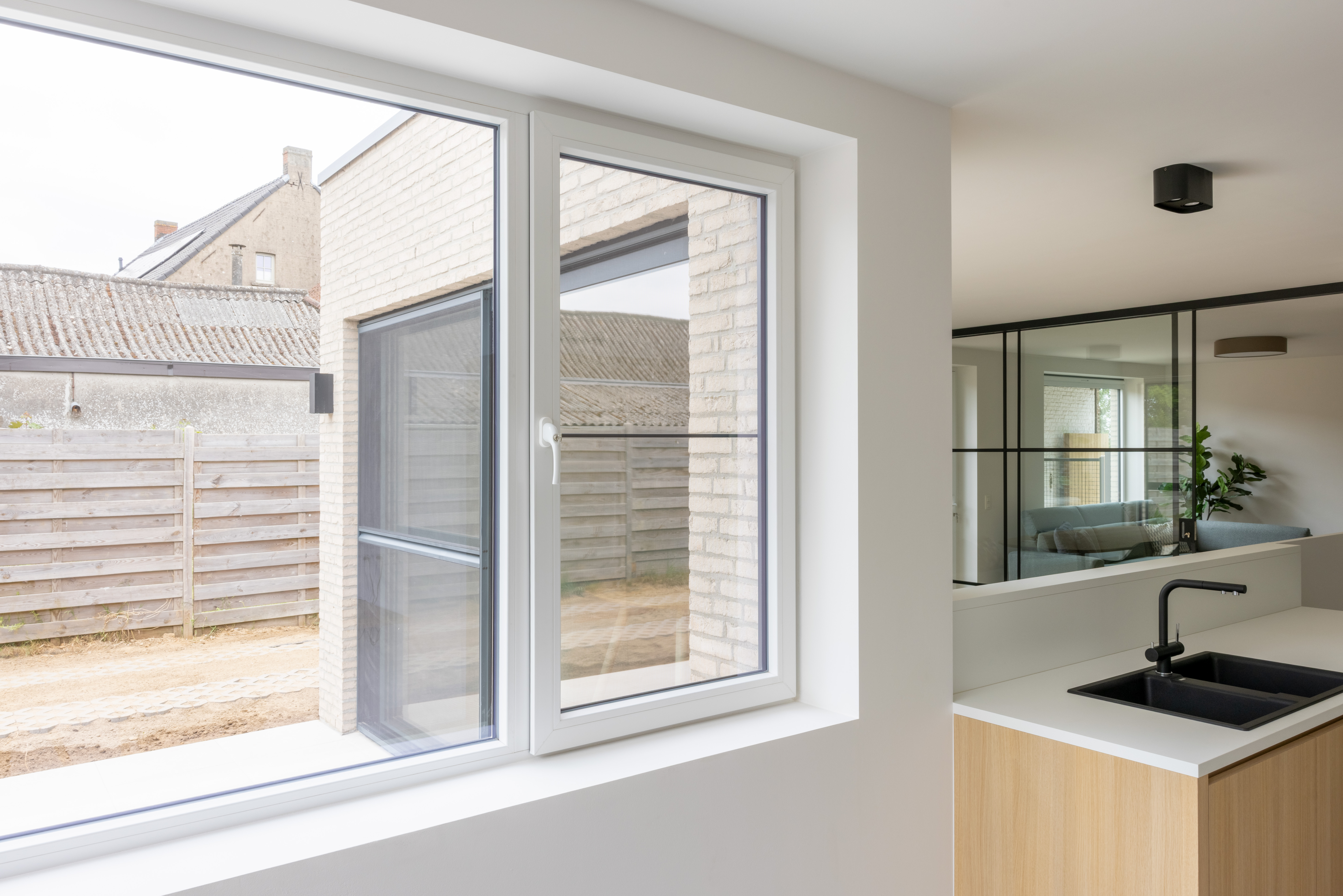Modern wit raam met vast deel en draai-kipraam in een gerenoveerde keuken, met uitzicht op aangrenzende woningen in gesloten bebouwing.