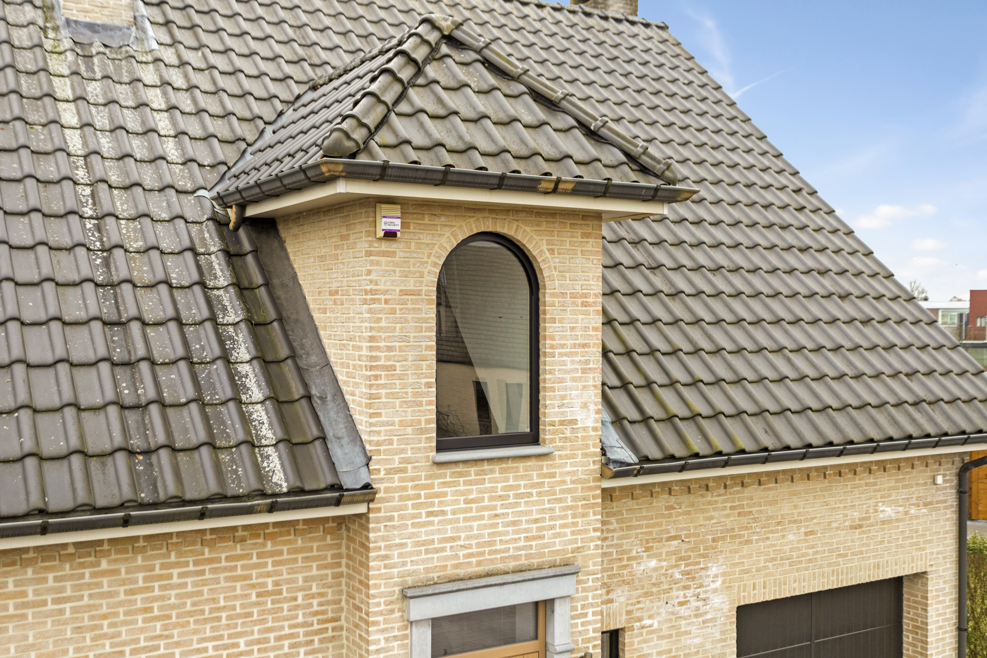 Vast, rond Impakt PLUS-raam met matzwart profiel in de lichte bakstenen gevel van een landelijk huis.