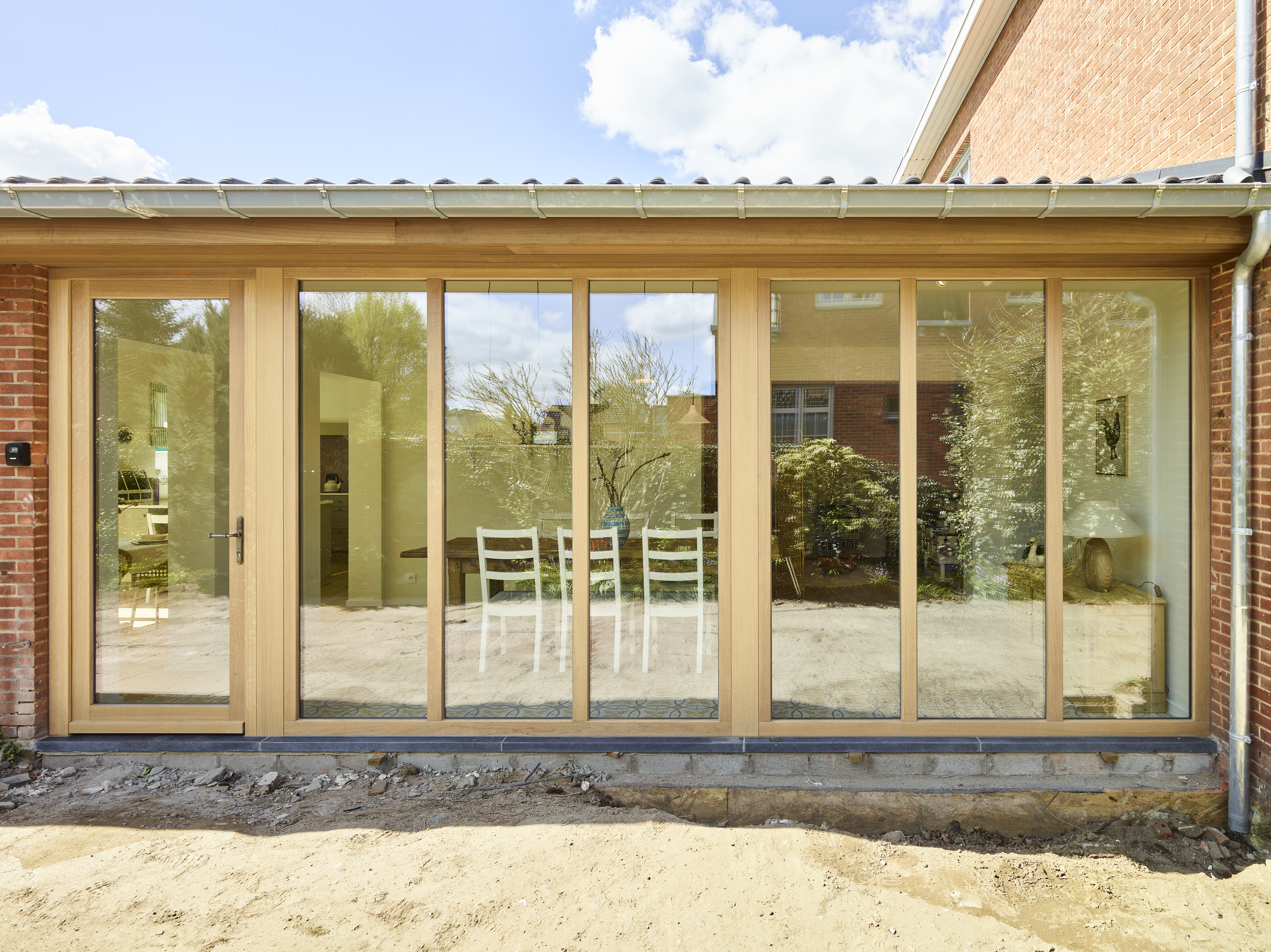 Modern raamgeheel in afgelakt lichteiken met driedubbele beglazing en beglaasde deur, geplaatst in een warme, landelijke bakstenen gevel.