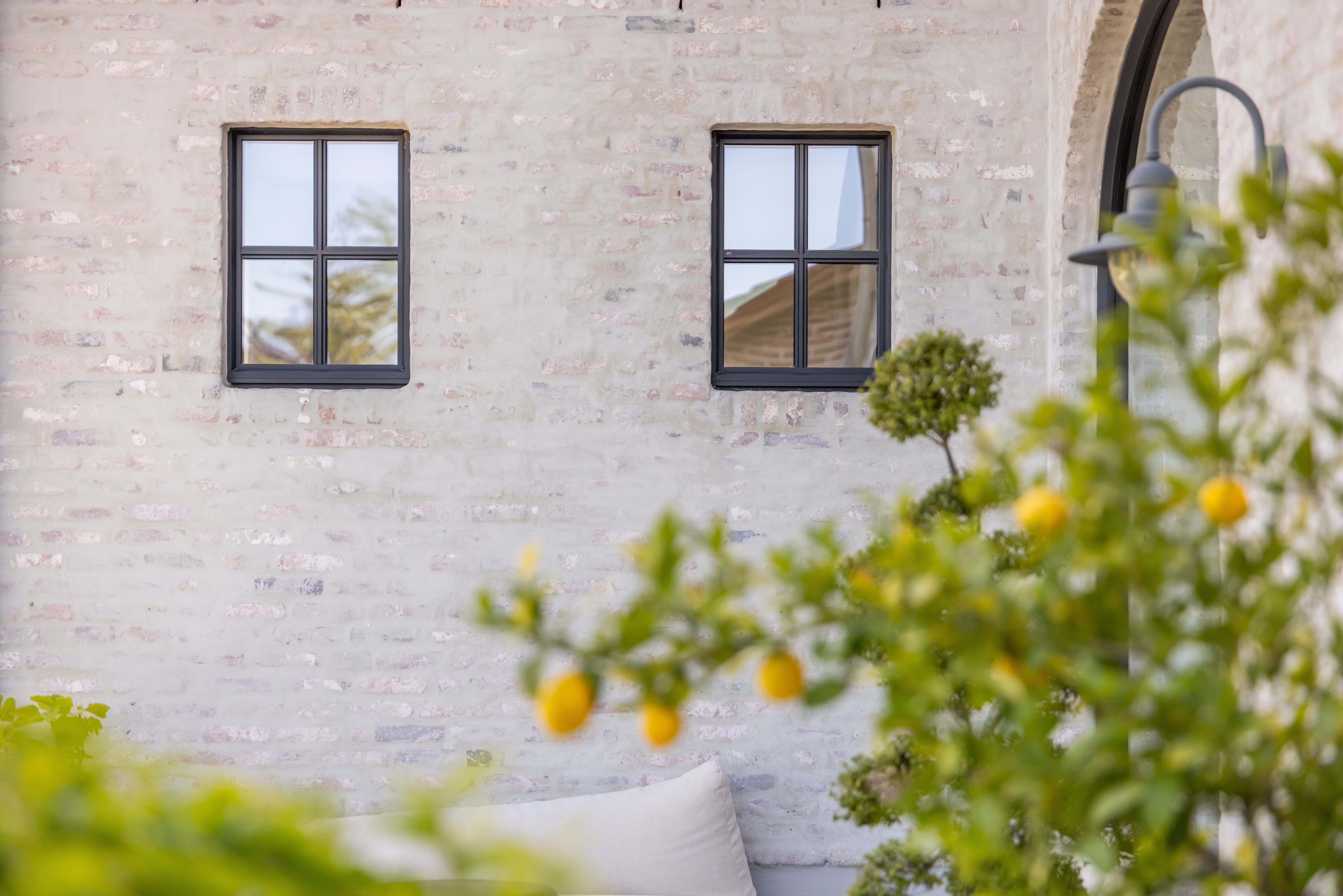 Twee zwarte draai-kipramen in Steellook PLUS small-stijl tekenen de lichte bakstenen gevel van een landelijke nieuwbouwwoning, omringd door verzorgd groen.