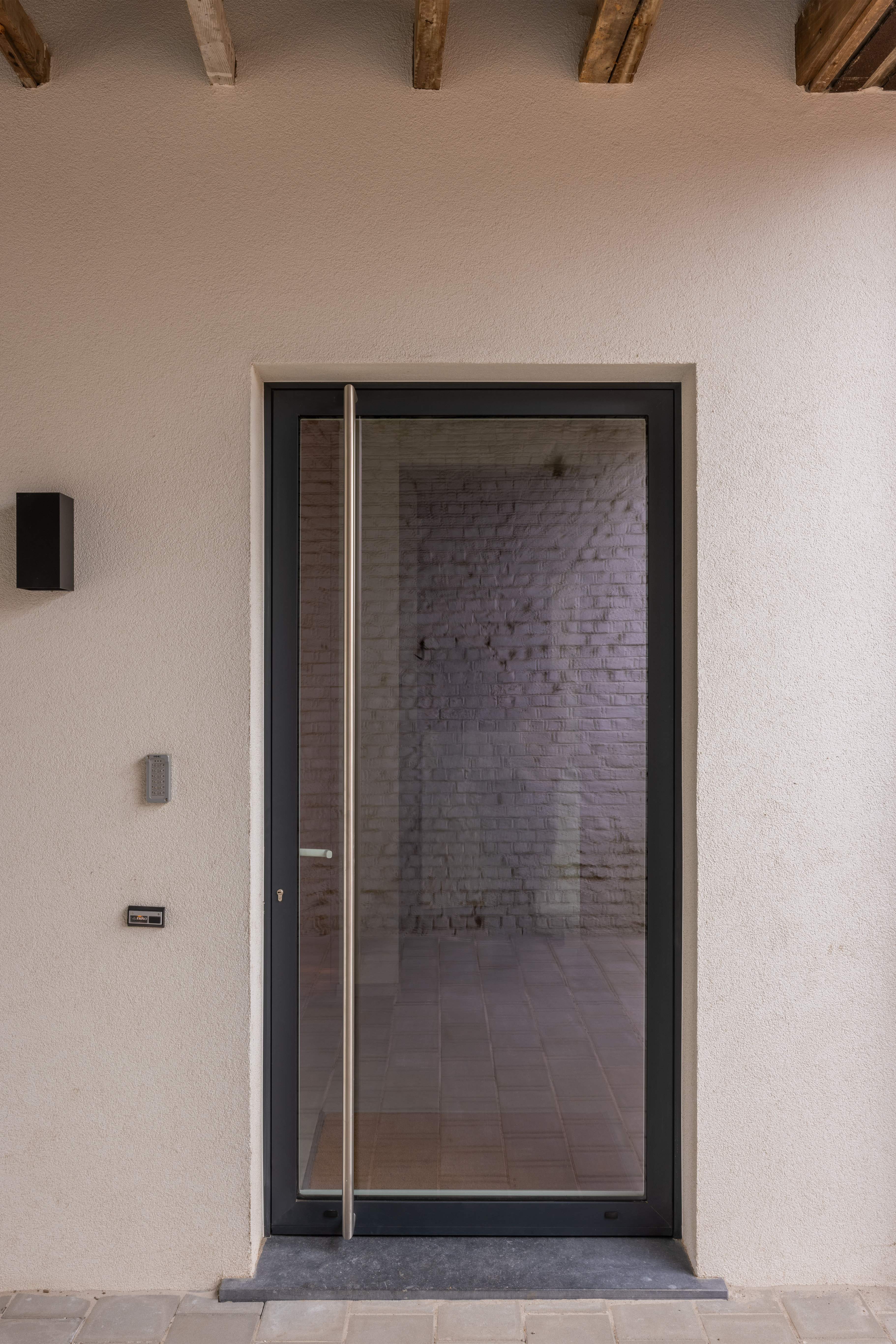 Moderne, volledig beglaasde aluminium voordeur in antracietgrijs met donker raamprofiel, geplaatst in de lichte gevel van een gerenoveerde rijwoning.