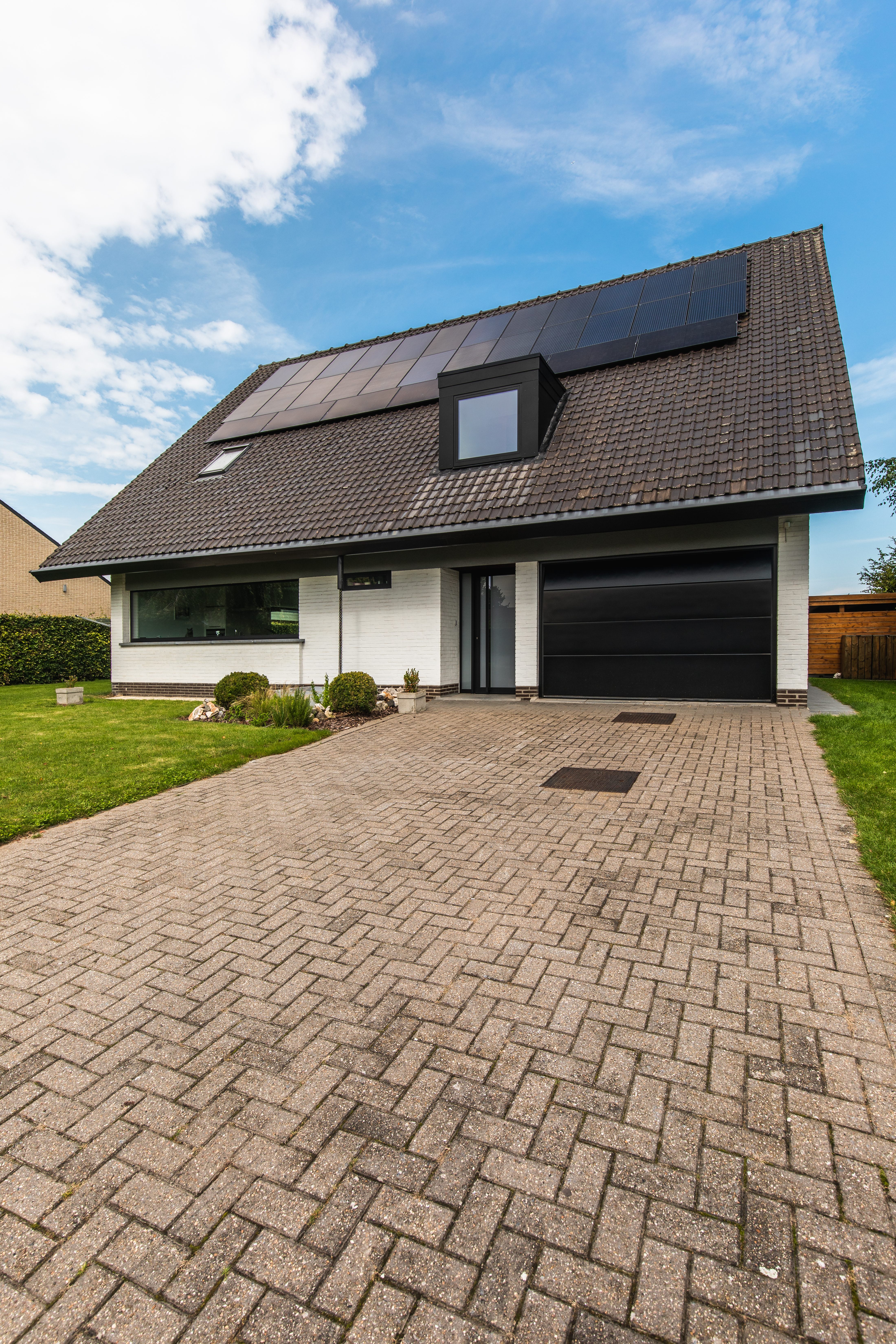 Moderne vrijstaande woning met een zwart vast raam naast een zwarte garagepoort, passend bij de gerenoveerde gevel en brede oprit.