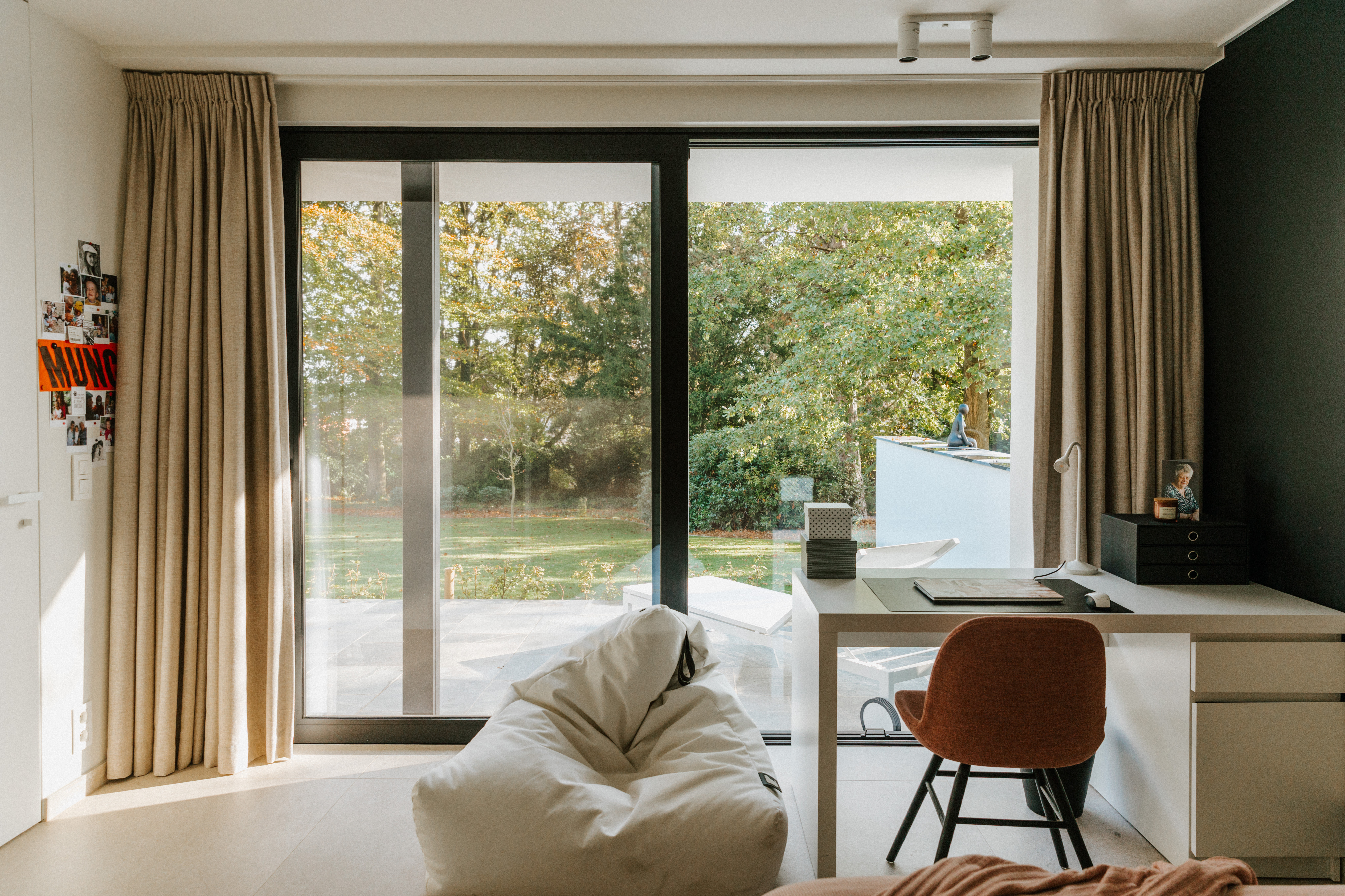 Modern gerenoveerde werkkamer met een zwart ALU Visoglide Monorail-schuifraam, een lichte zitzak, een bureau en uitzicht op de tuin.