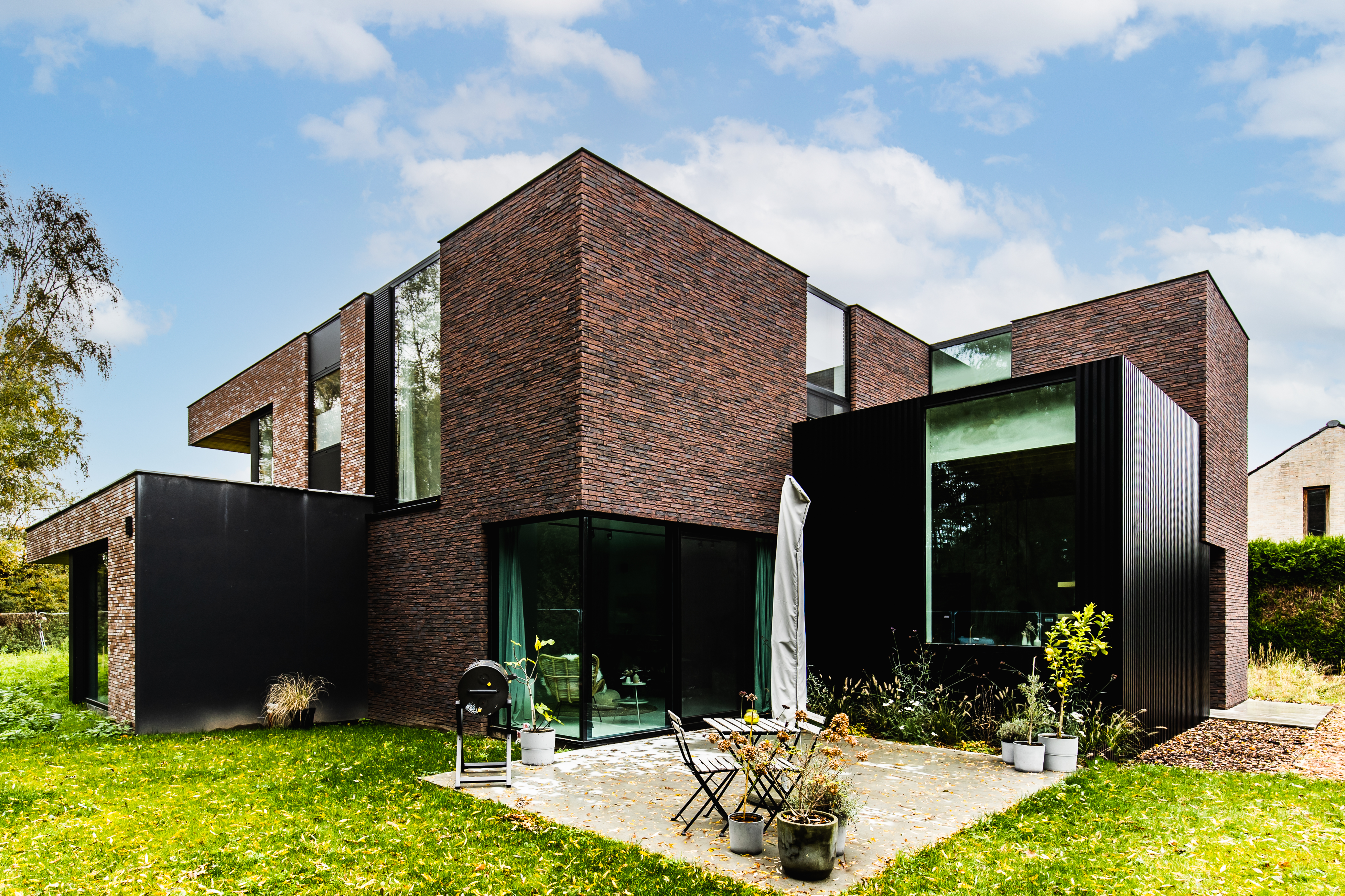 Karaktervolle, moderne vrijstaande woning in baksteen met zwarte raamprofielen, grote glaspartijen en een klein terras in de groene tuin.