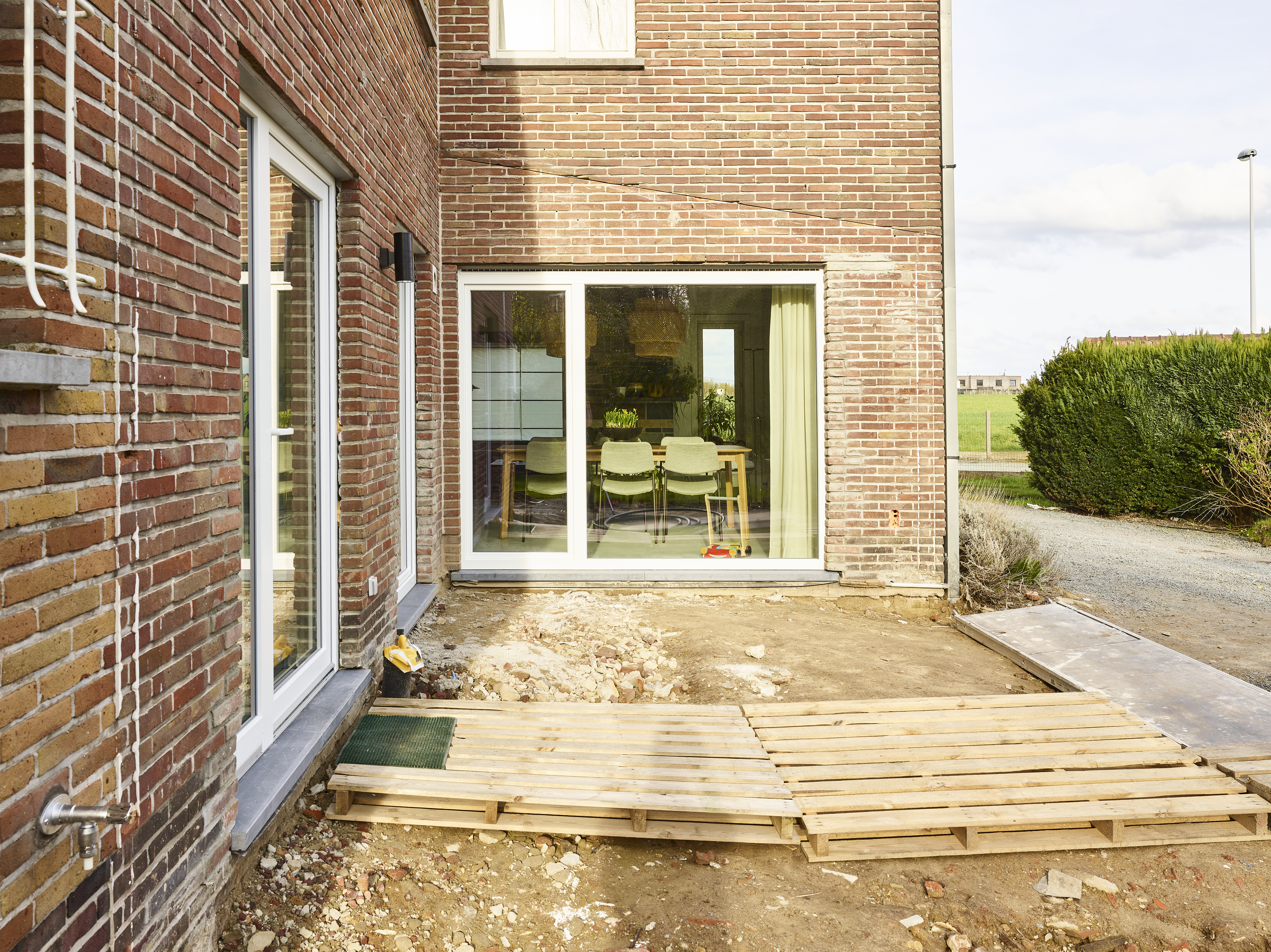 Witte Komfort PLUS-draai-kipramen en vaste ramen in een bakstenen gevel, met zicht op het interieur en een gedeeltelijk aangelegd houten terras.