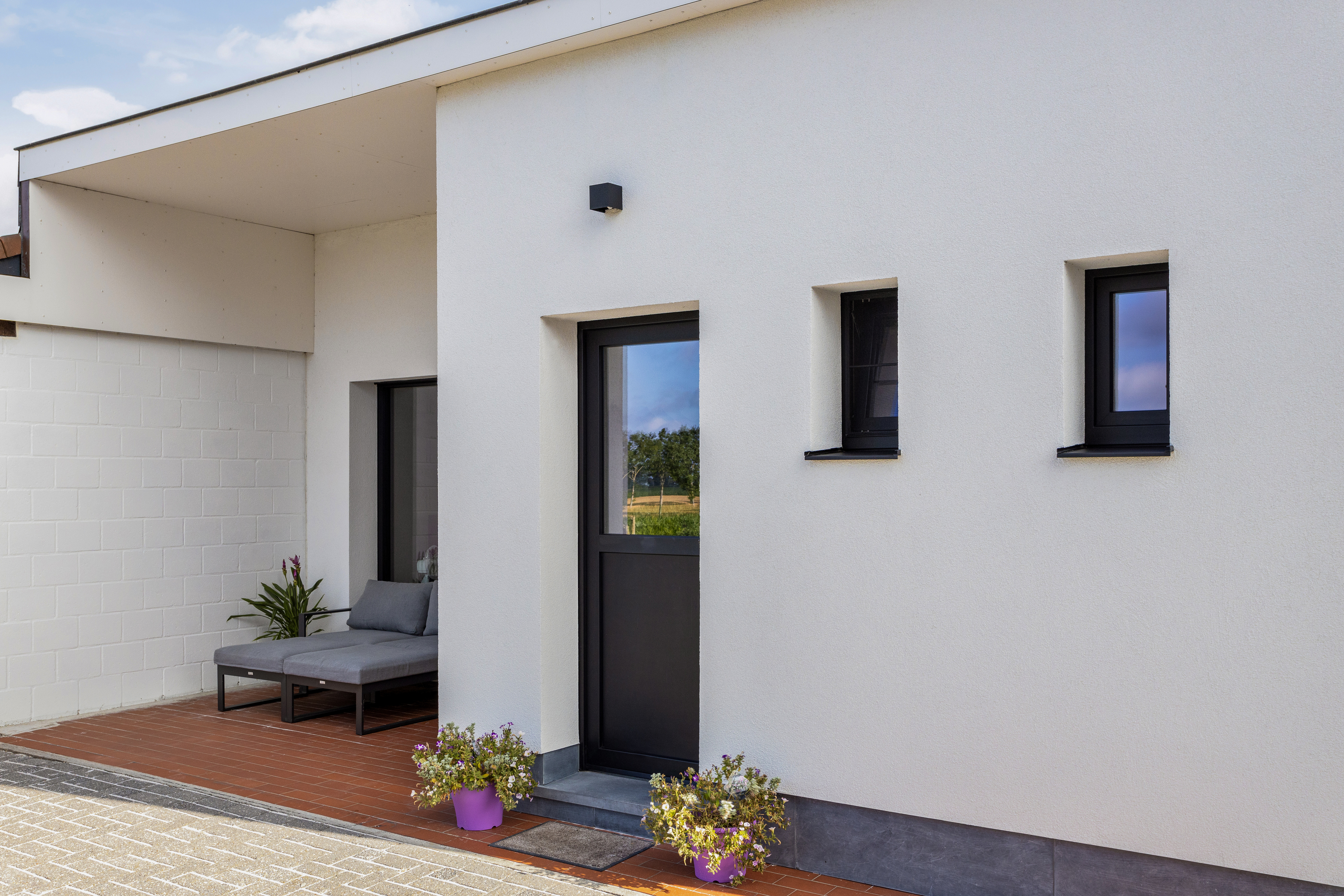 Modern gerenoveerde woning met matzwarte PVC-draai-kipramen en een semi-beglaasde deur in een lichte gevel, naast een overdekt terras.