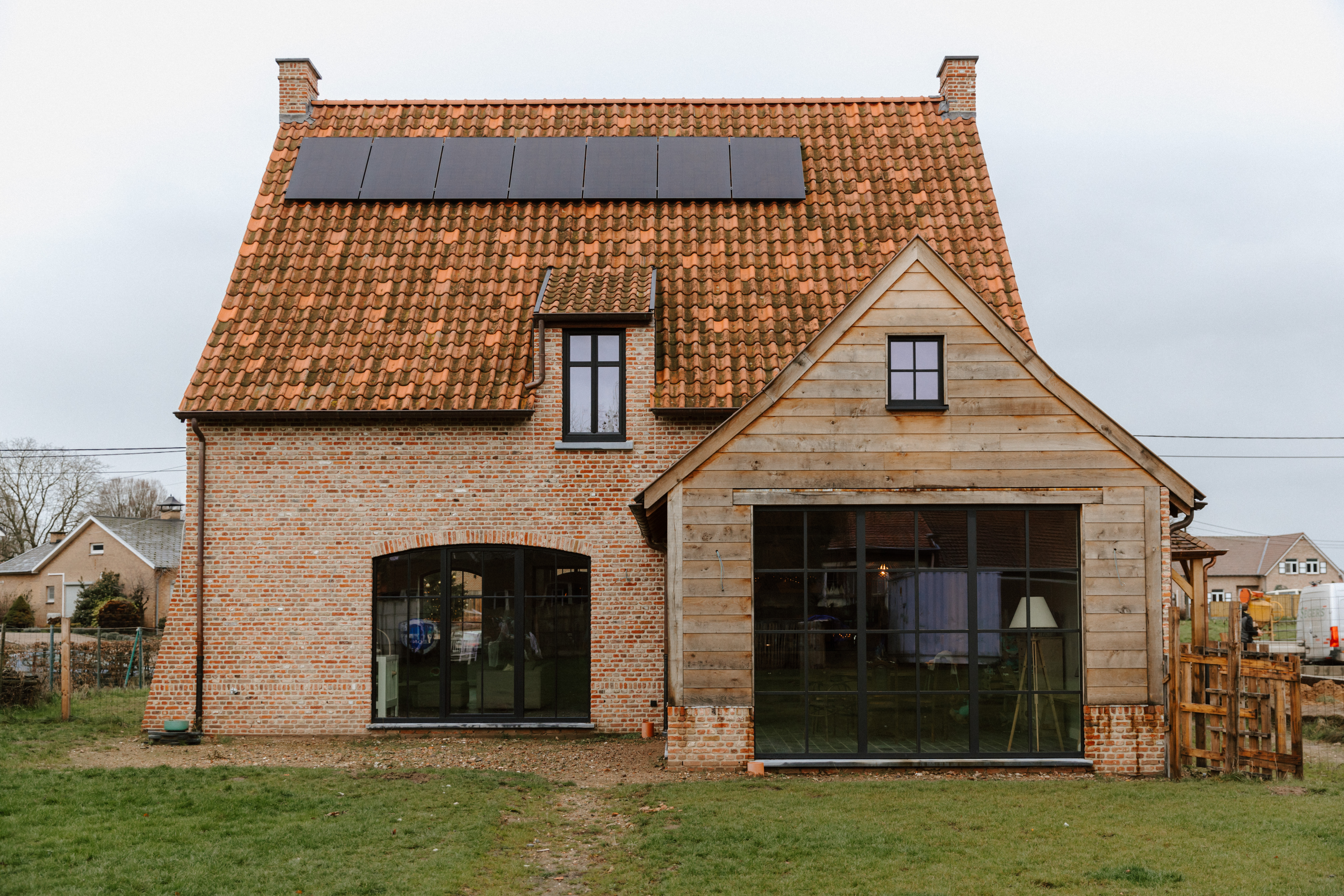 Landelijke bakstenen woning met matzwarte ramen met driedubbele beglazing, vaste ramen en draai-kipramen, aangevuld met een houten aanbouw.