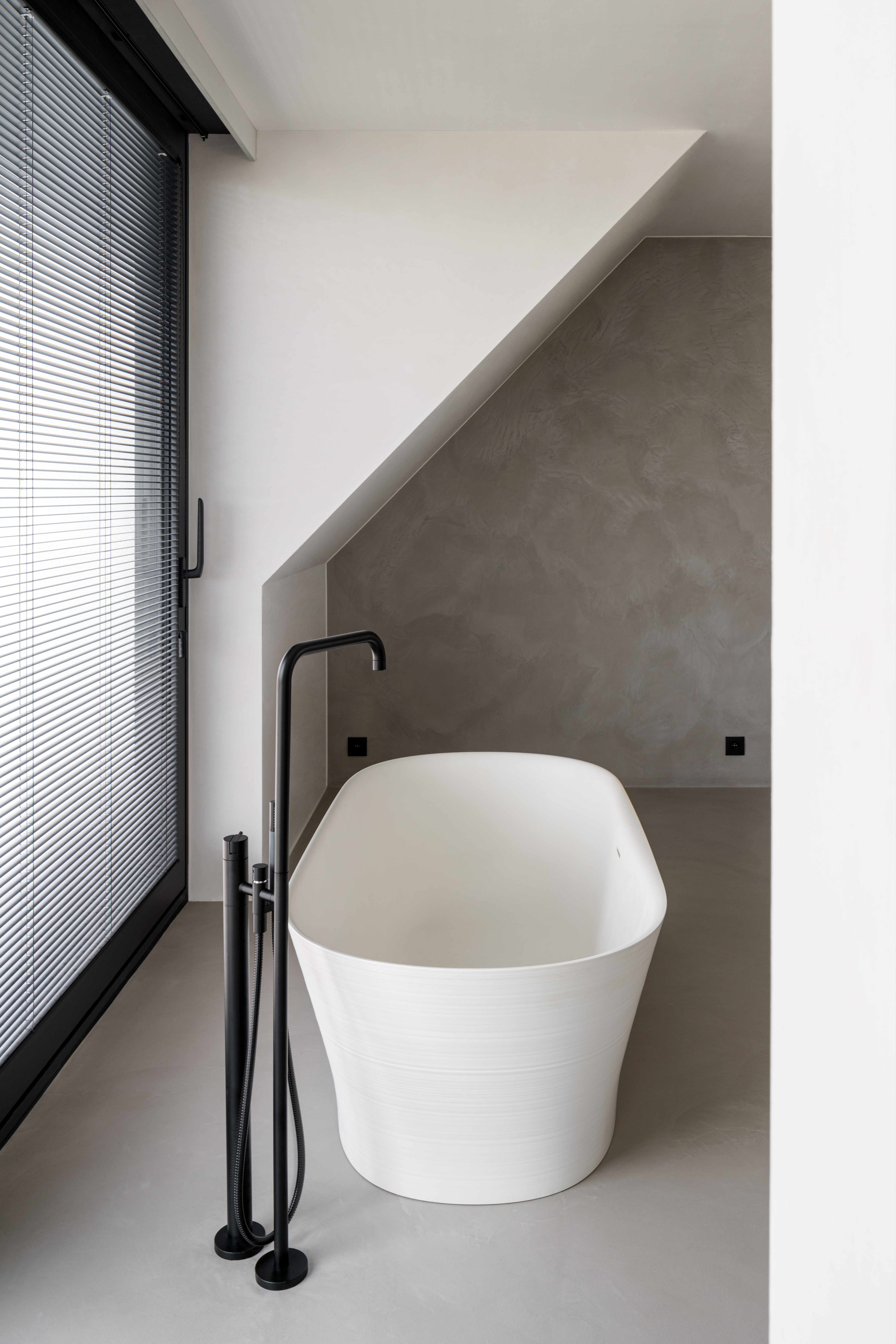 Moderne badkamer in een nieuwbouwwoning met vrijstaand bad, zwarte kraan en zwart aluminium ALU Ultraglide Monorail-schuifraam.