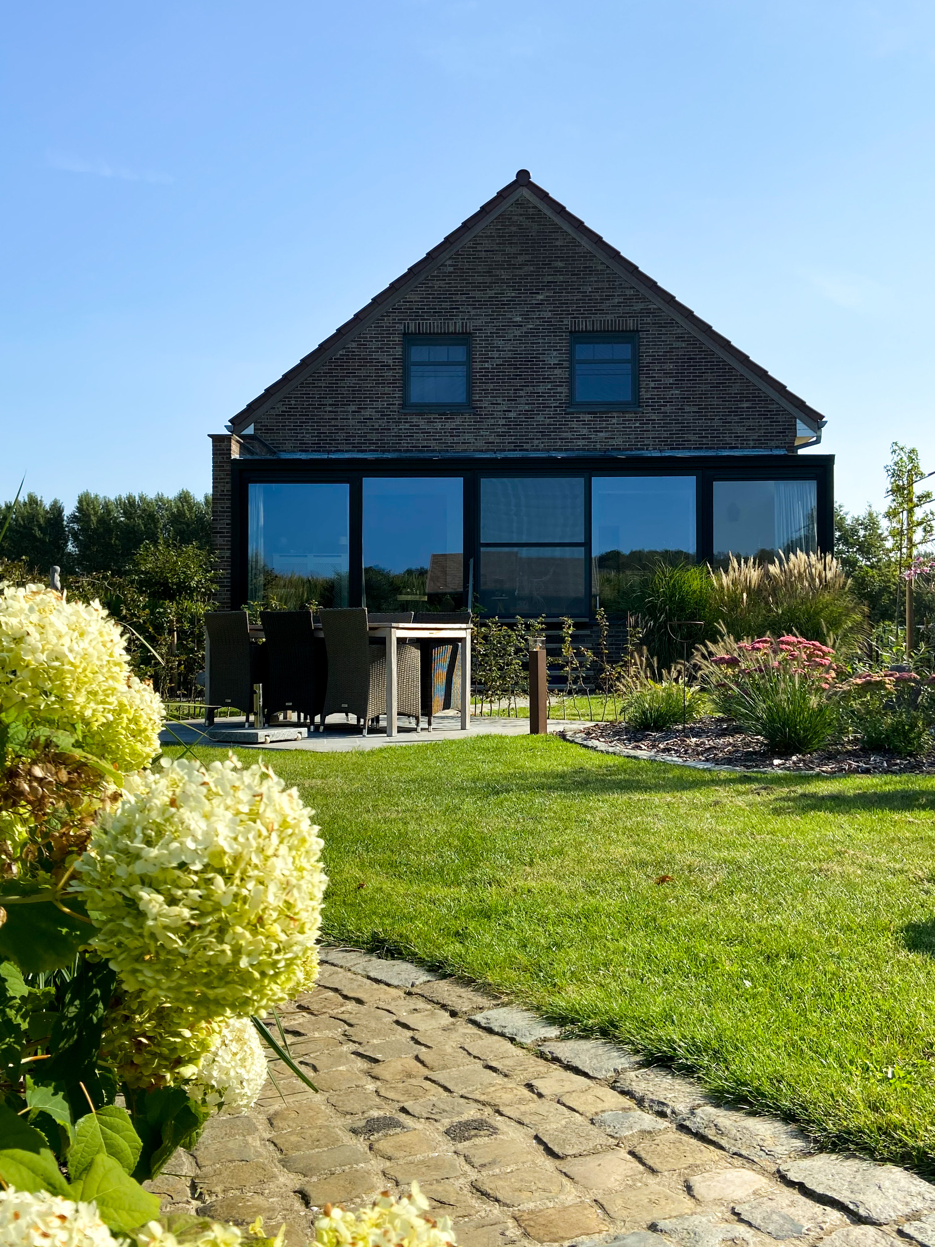 Gerenoveerde vrijstaande woning met kwartsgrijze raamprofielen en een schuifvliegenraam, grote glaspartijen en een verzorgde tuin met terras.