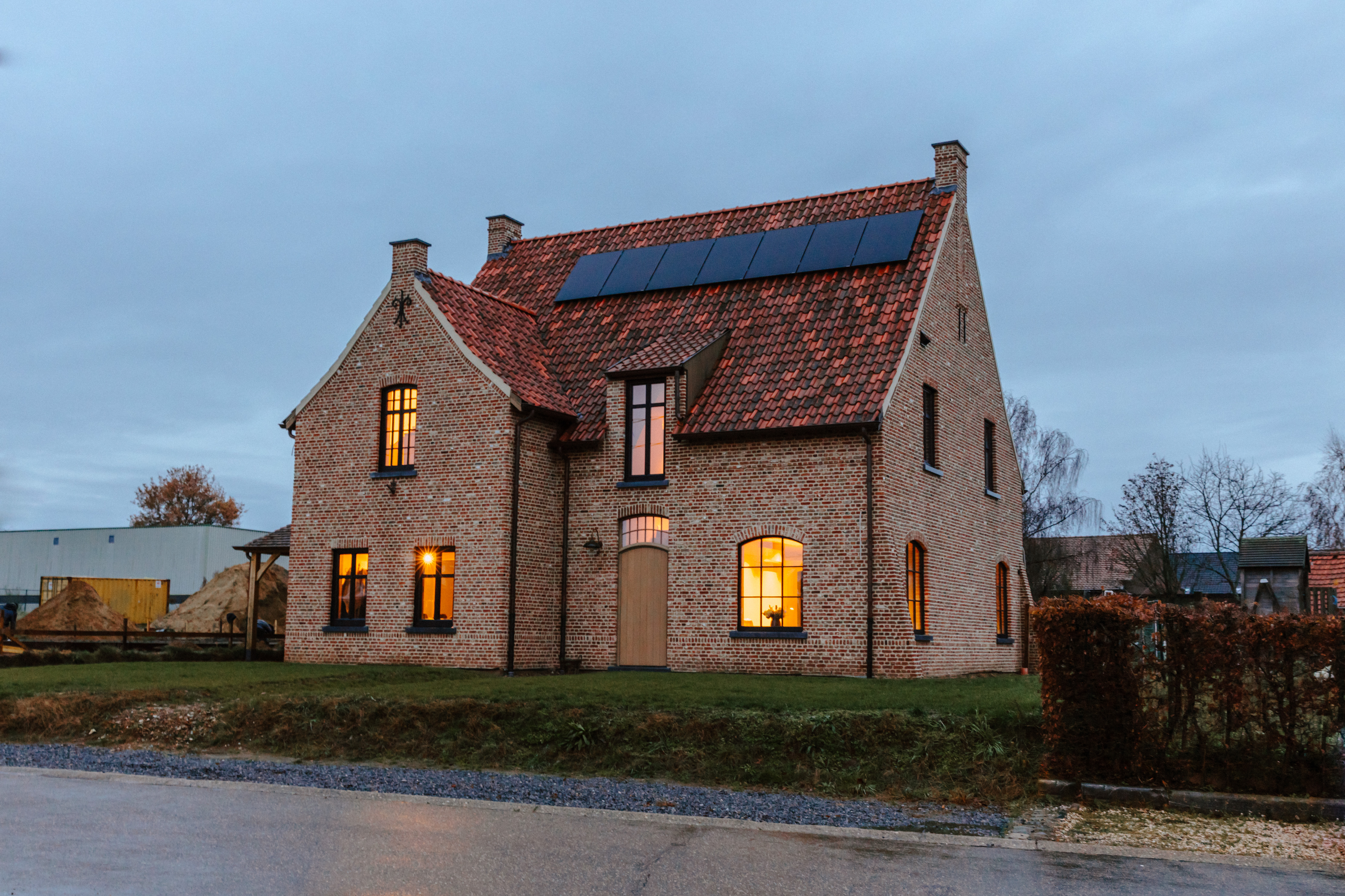 Landelijke bakstenen woning met matzwarte ramen in Afrormosia, een vast raam en een dubbel raam naast een deur met bovenlicht.