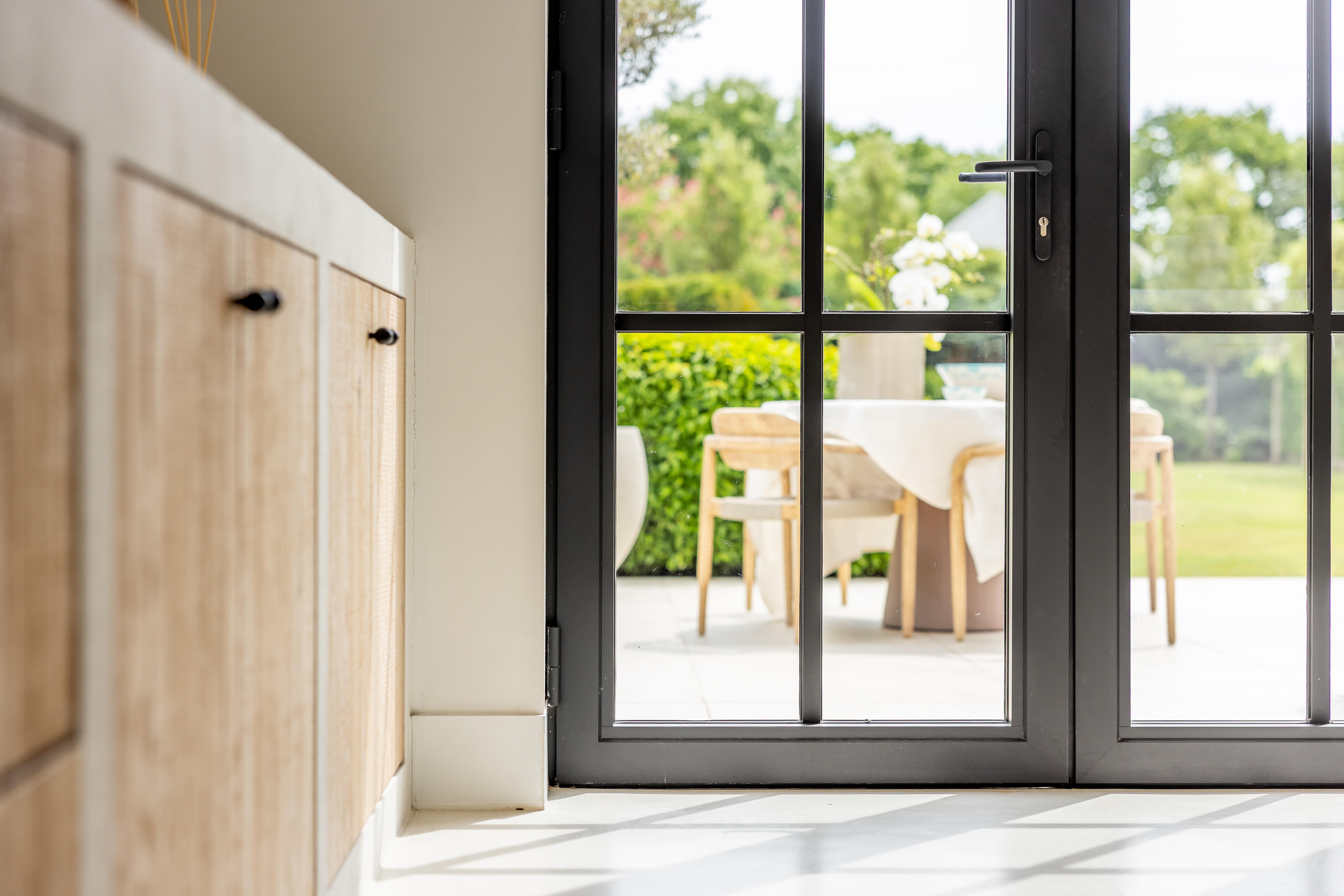 Zwarte deur in staal-look met glasvakken naast een passend raam, van een landelijke nieuwbouwwoning naar het terras en de tuin.