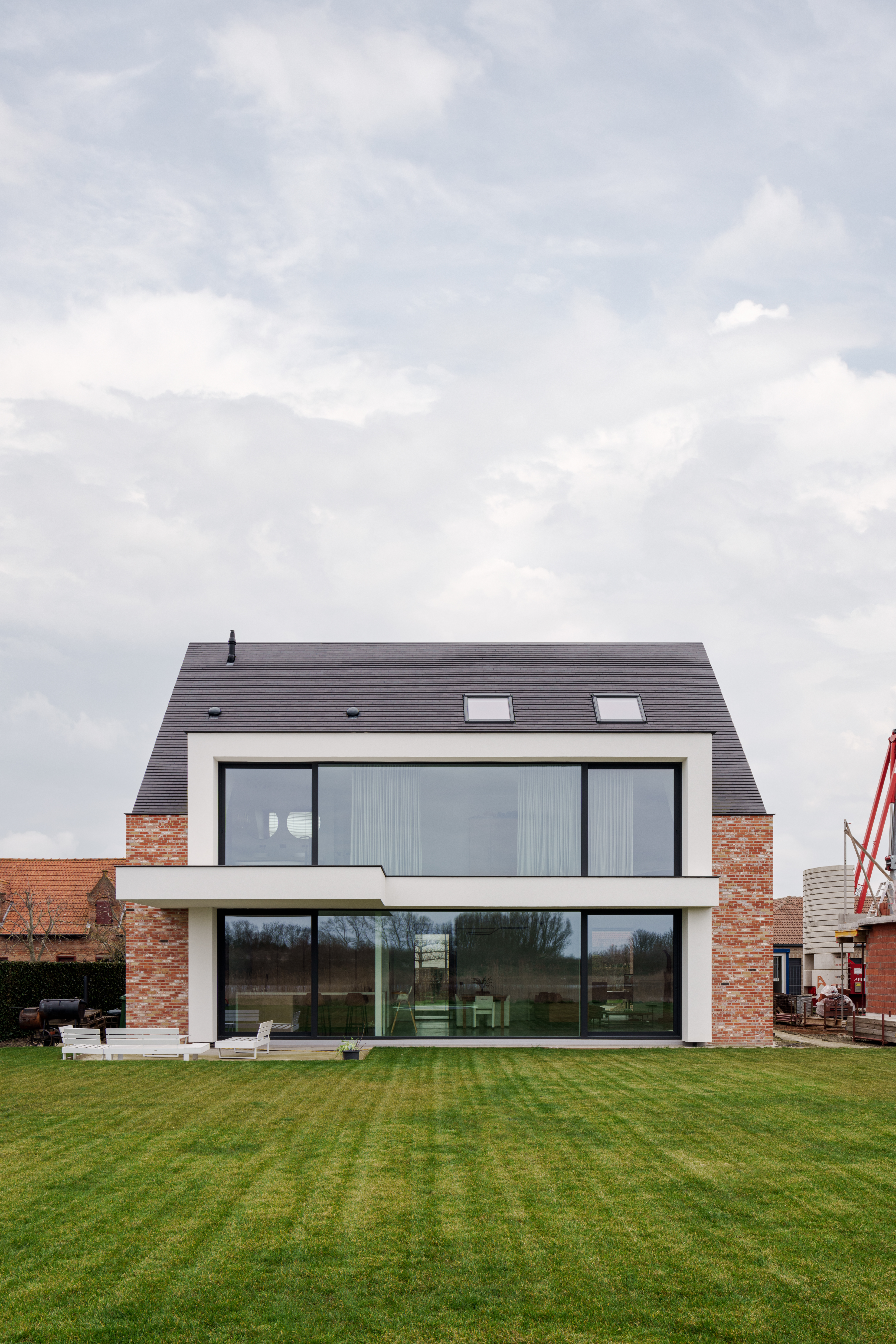 Moderne vrijstaande nieuwbouwwoning met grote zwarte aluminium schuiframen van het type ALU Ultraglide Monorail, met een ruime grasweide ervoor.