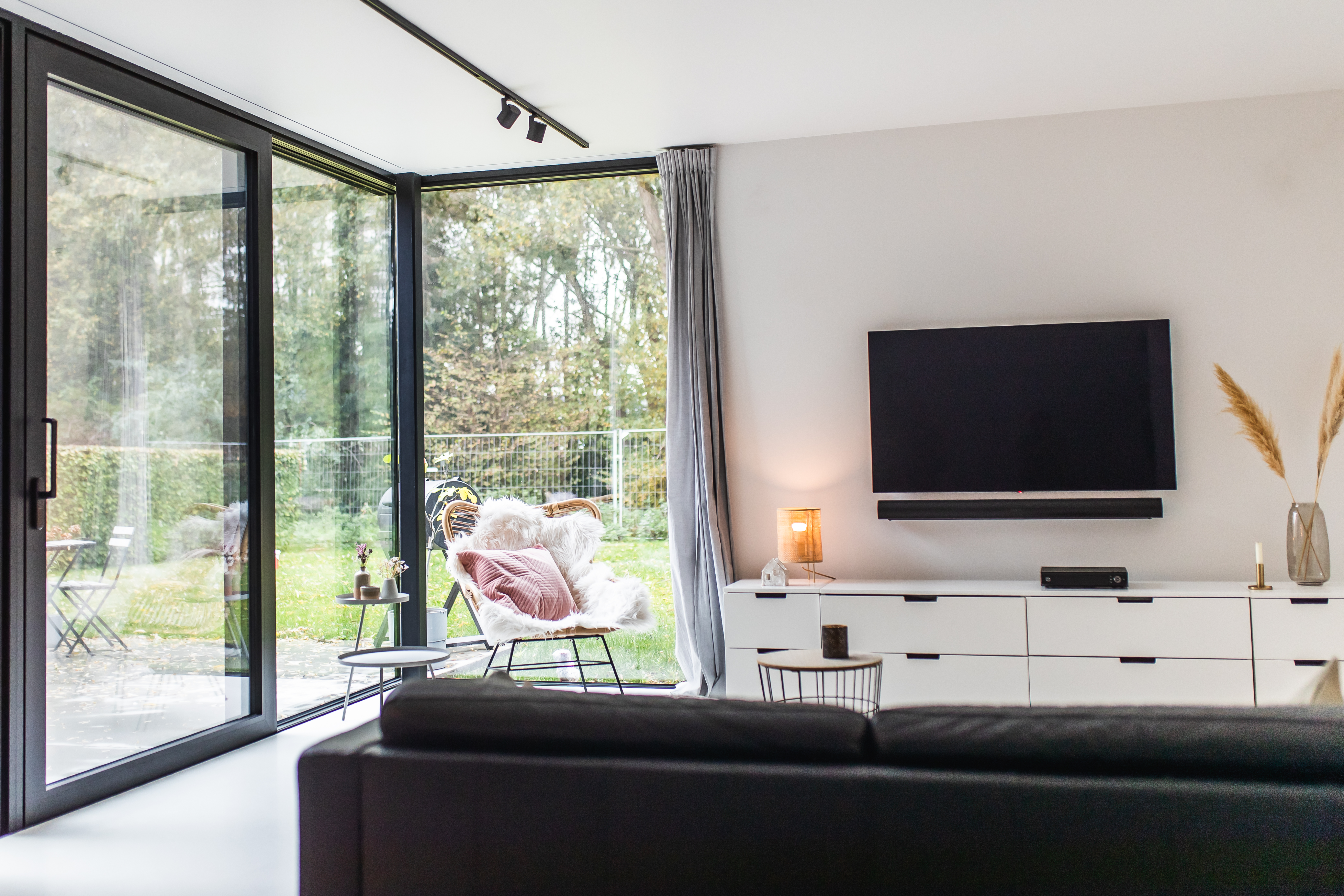 Zwart aluminium schuifraam in de moderne leefruimte van een nieuwbouwwoning in open bebouwing, met zicht op de tuin en een strak interieur.