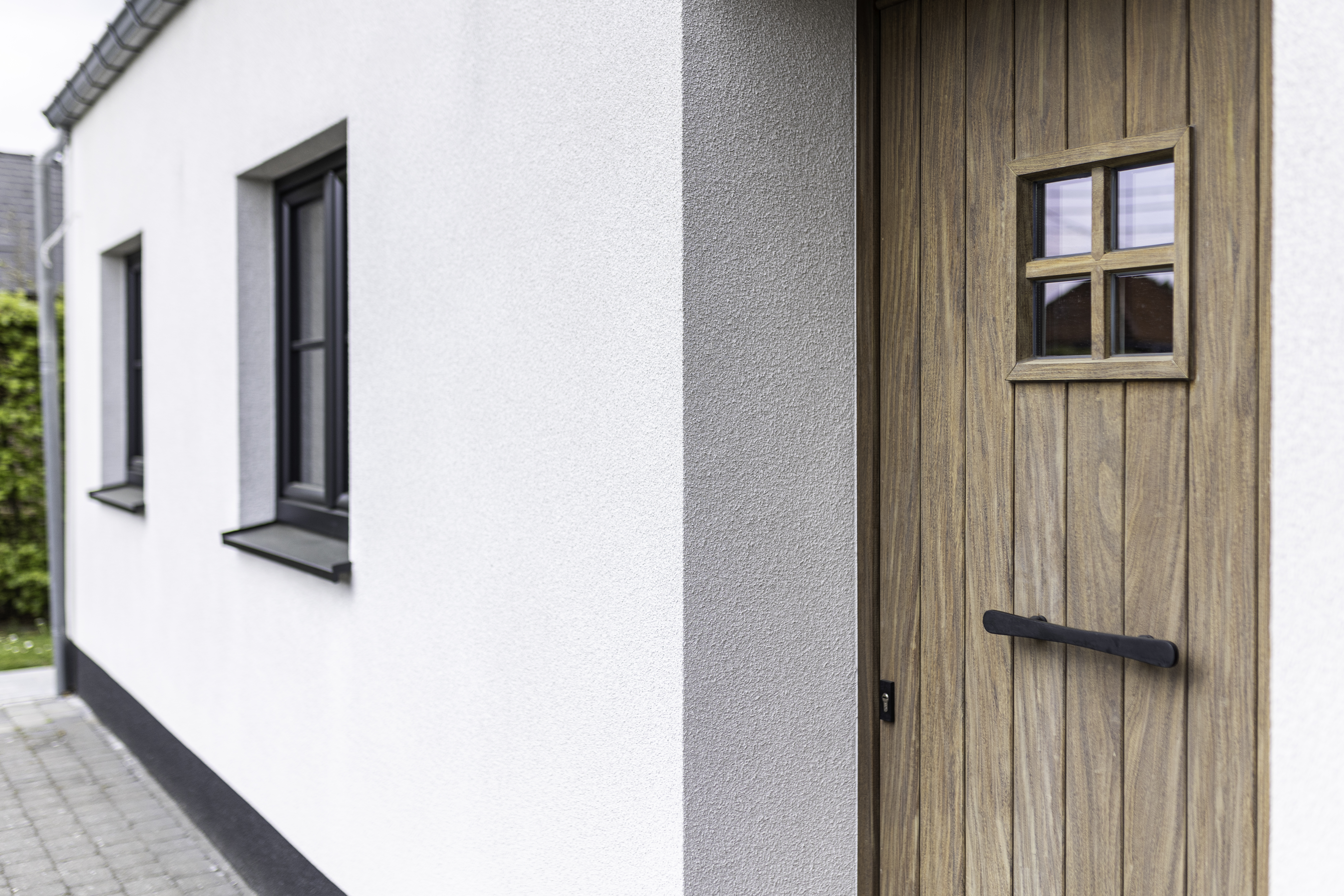 Gerenoveerde vrijstaande woning met een dubbel raam en een deur in afgelakt Afrormosia, met matzwarte raamprofielen.