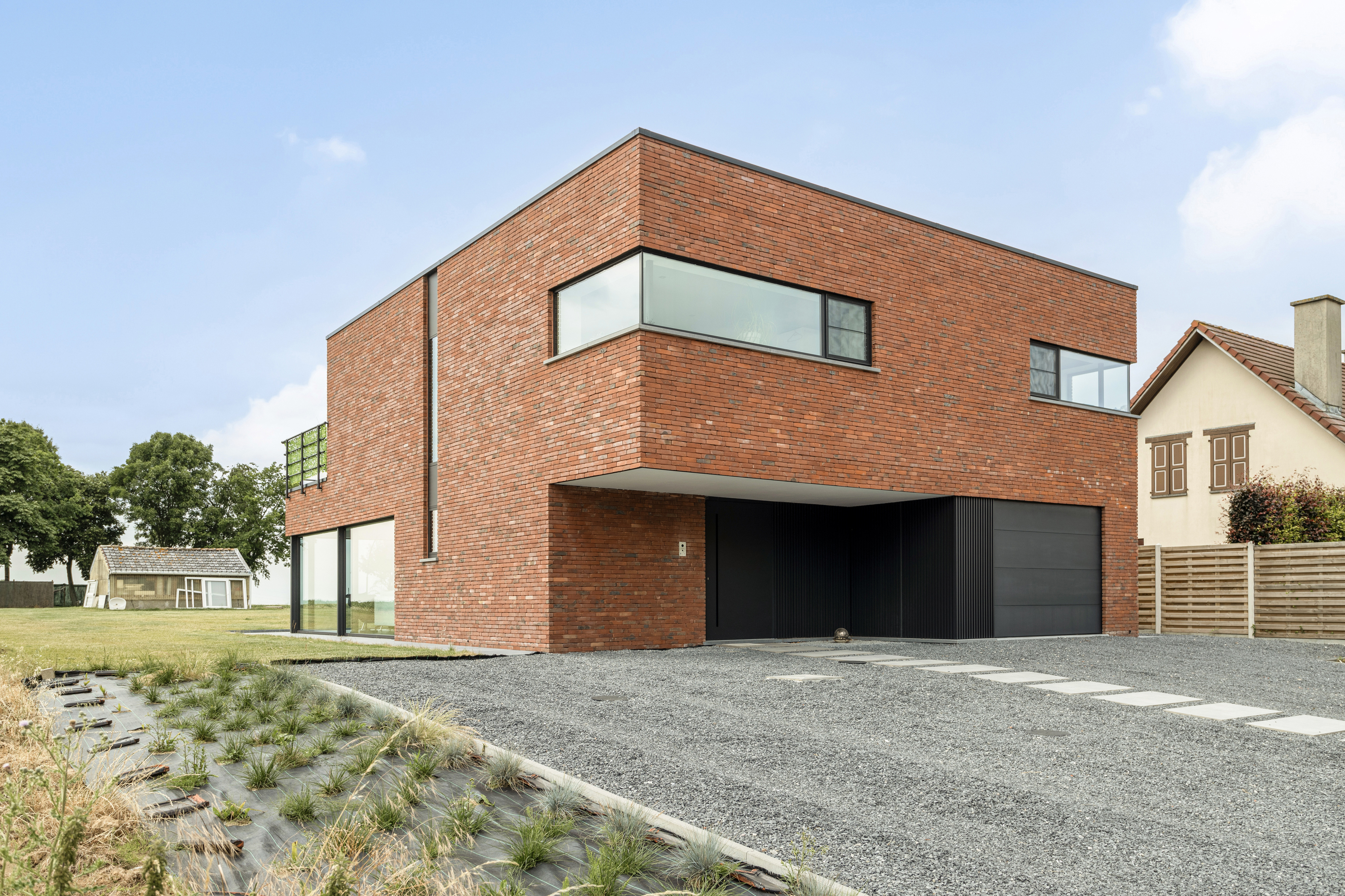 Moderne vrijstaande bakstenen nieuwbouwwoning met zwarte hoekramen en vaste ramen, een overdekte oprit en een donkere garagepoort.