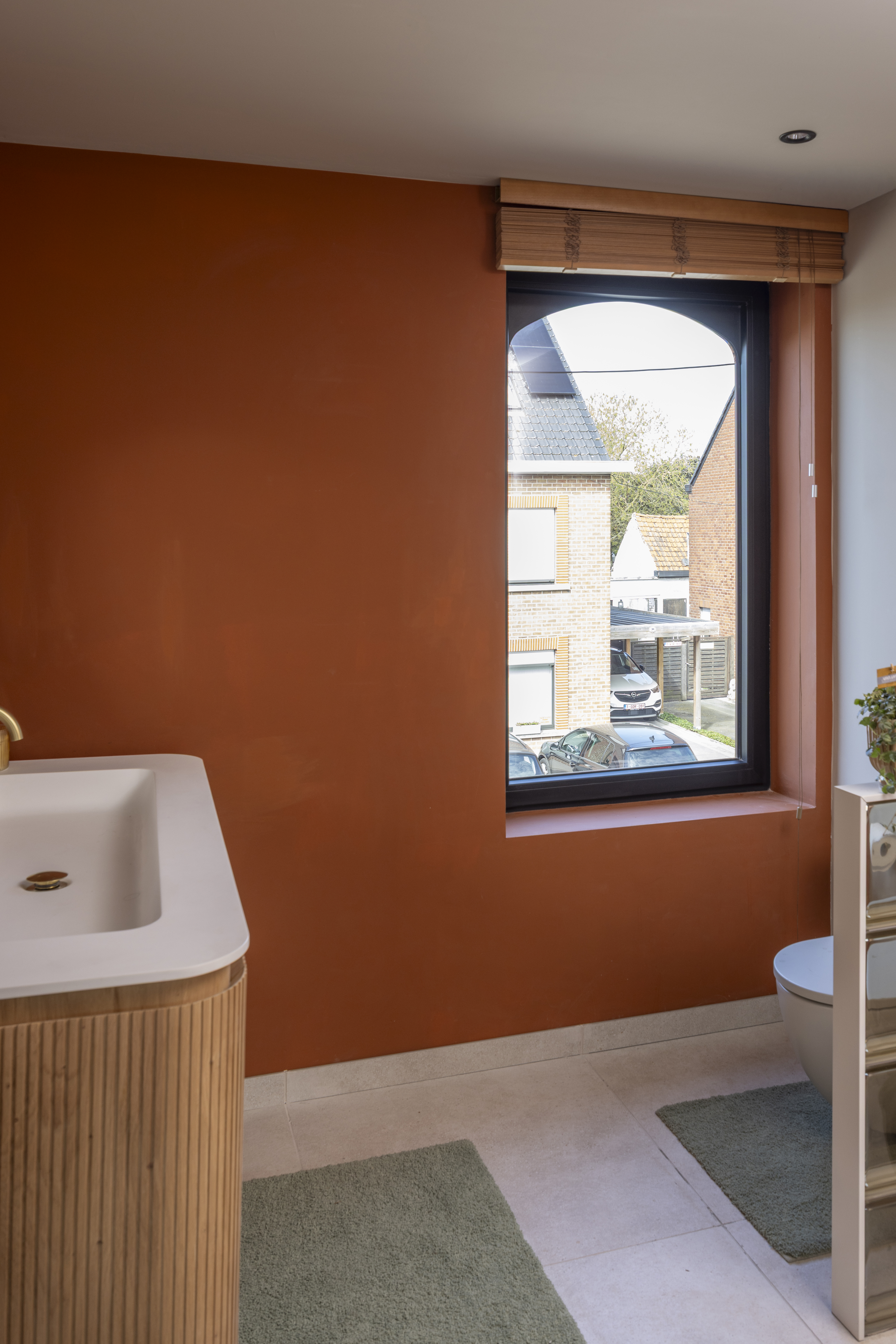 Zwart mat draai-kipraam uit de Komfort PLUS-reeks in een terracottakleurige binnenmuur, met zicht op de omliggende huizen.