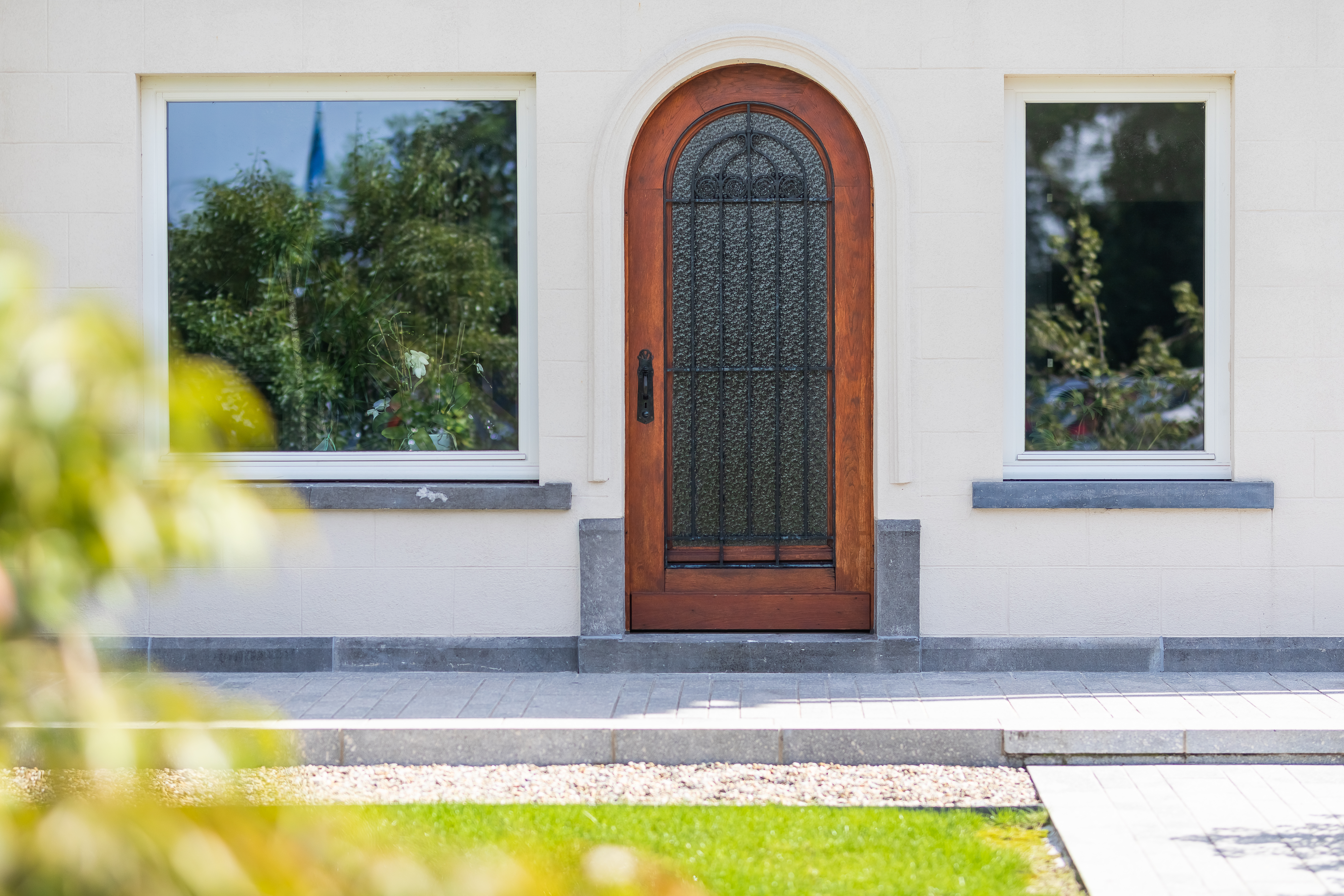 Witte voorgevel van een gerenoveerde vrijstaande woning in verfijnde klassieke stijl, met een gebogen houten voordeur en twee ramen met witte raamprofielen.