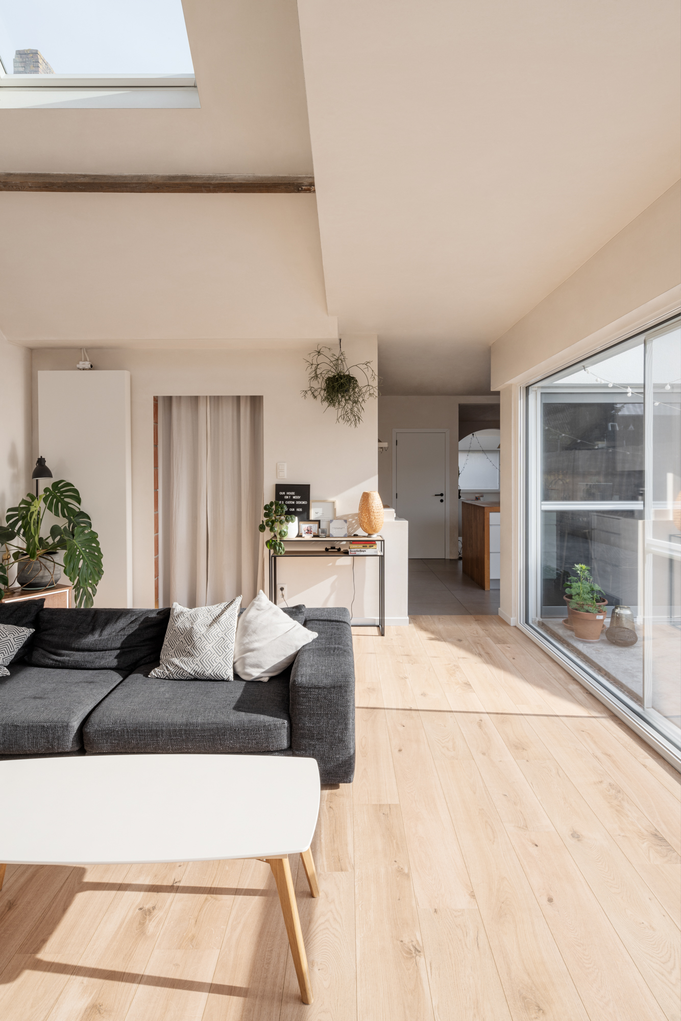 Licht interieur met een groot vast raam in verkeerswit aluminium, naast een glazen schuifpartij, in een gerenoveerde woning.