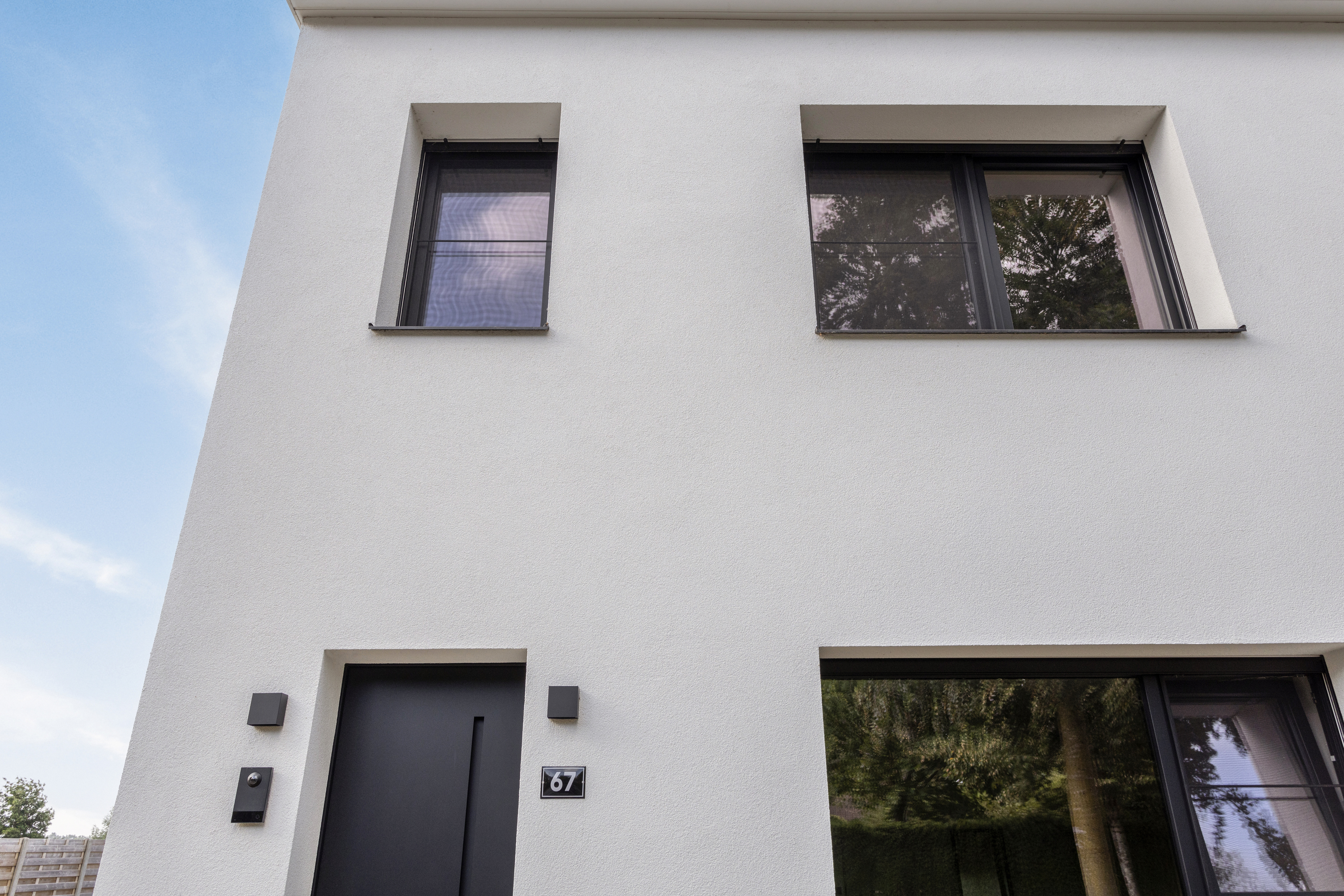 Modern, wit bepleisterd huis met matzwarte pvc-ramen: een draai-kipraam en een dubbel raam met vliegenraam.
