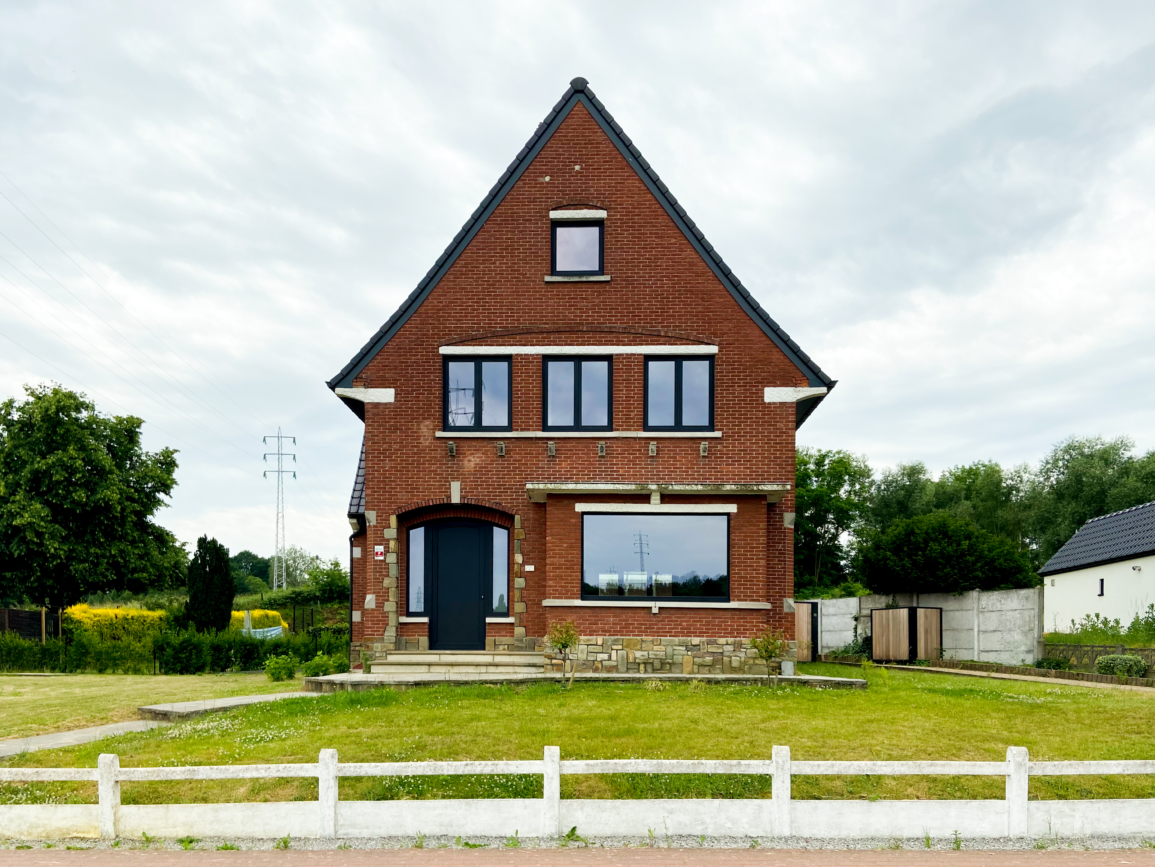 Vrijstaande bakstenen woning met matzwarte raamprofielen, een voordeur met dubbele zijlichten en een groot raam met paneel aan de voorgevel.