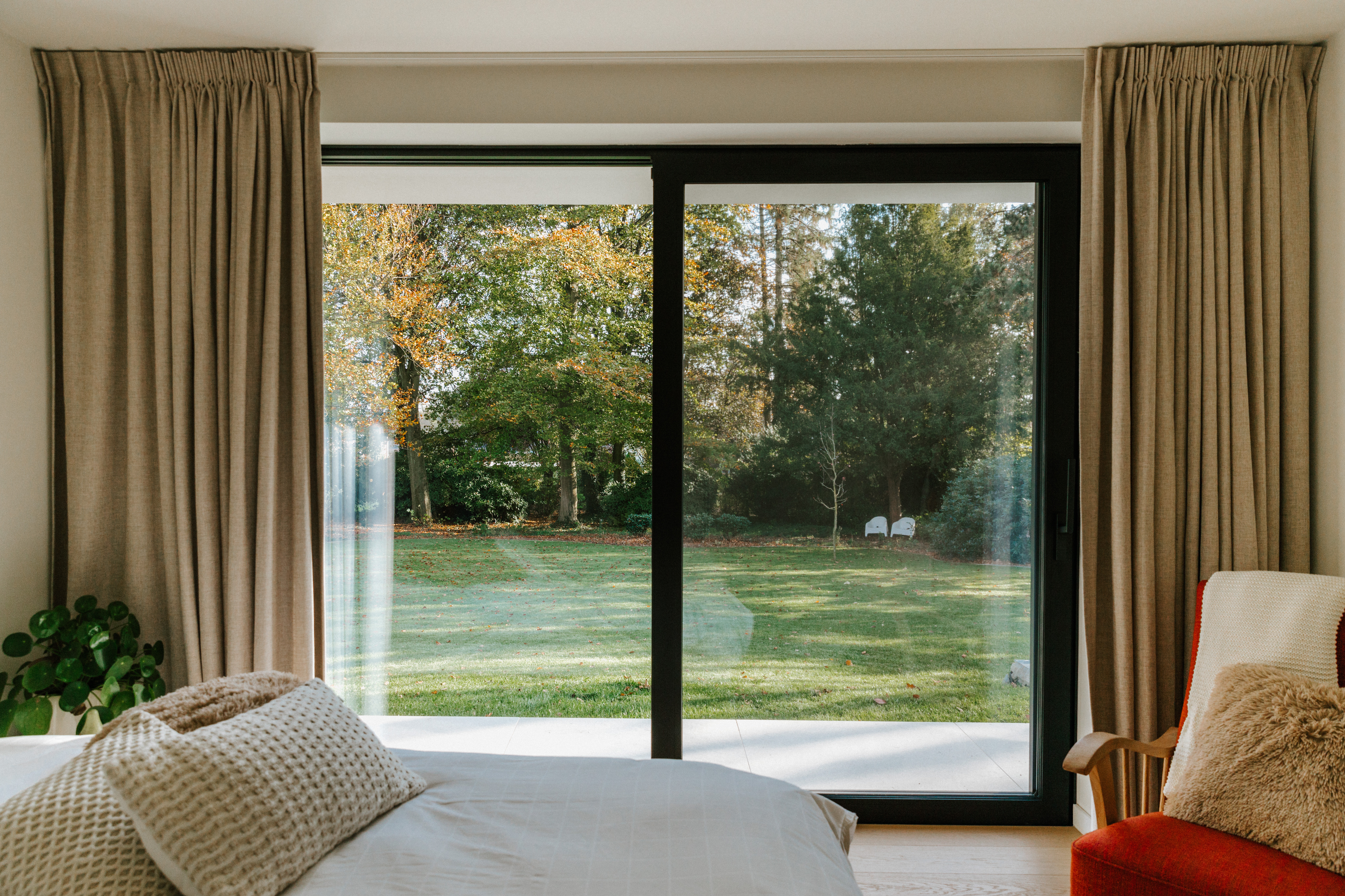 Modern gerenoveerde slaapkamer met een zwart ALU Visoglide Monorail-schuifraam in signaalzwart en uitzicht op een groene tuin.