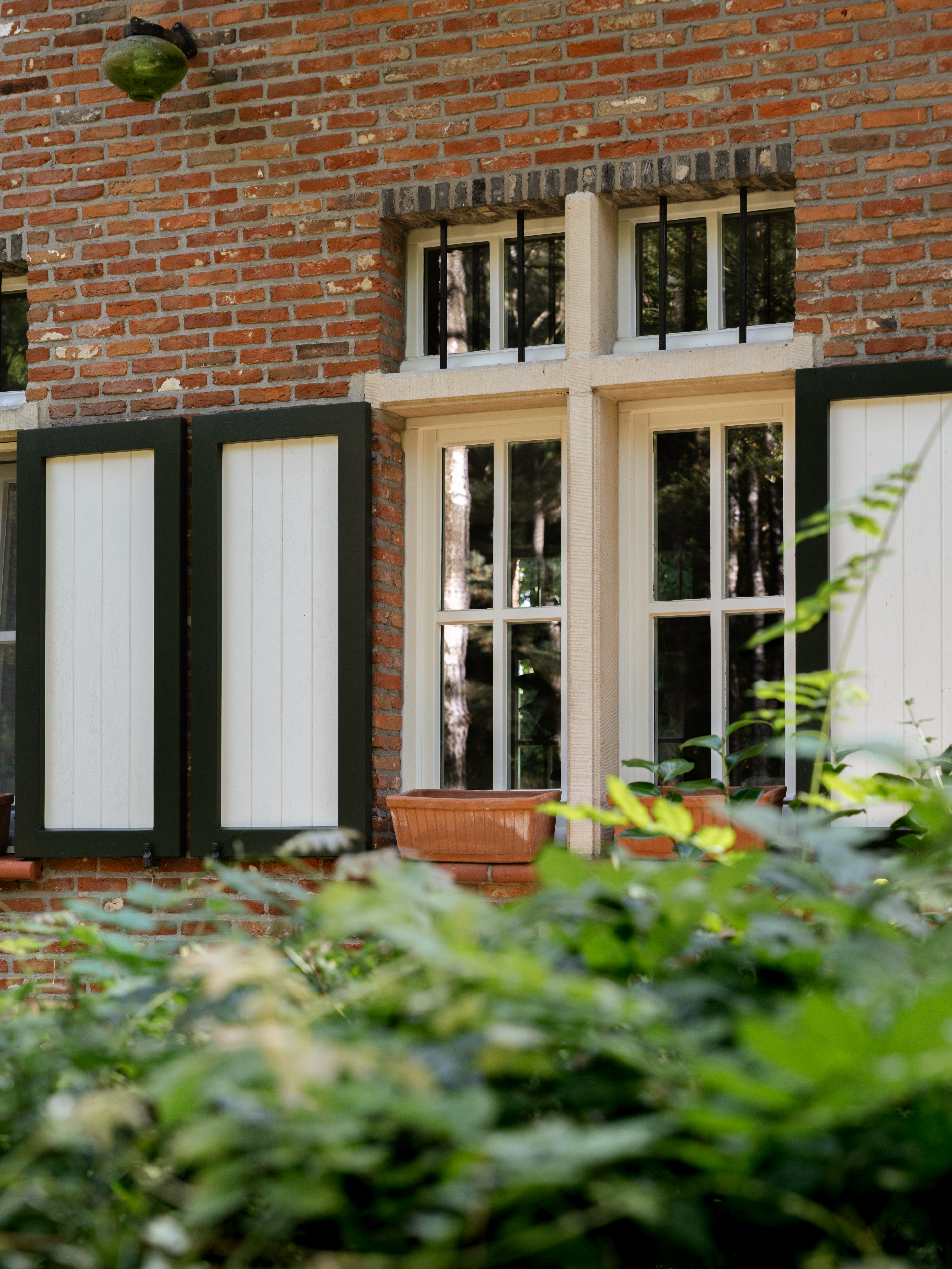 De landelijke vrijstaande woning heeft lichte raamprofielen met zwarte luiken in een rode bakstenen gevel, passend bij een warme, gerenoveerde uitstraling.
