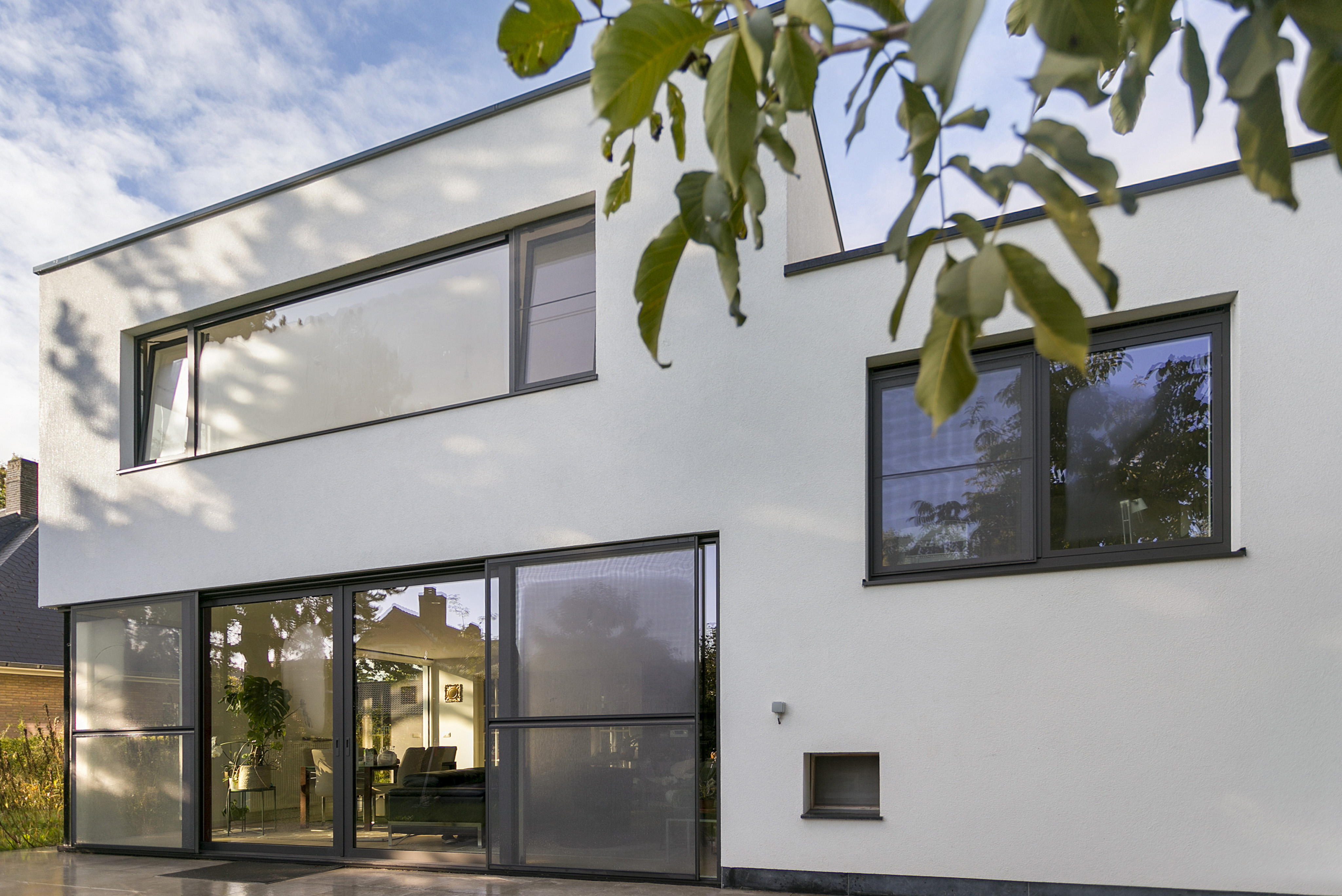 Moderne woninggevel met grijsbruine aluminium ramen, waaronder een groot schuifraam met vliegenraam, vaste ramen en draai-kiepramen in verschillende formaten.