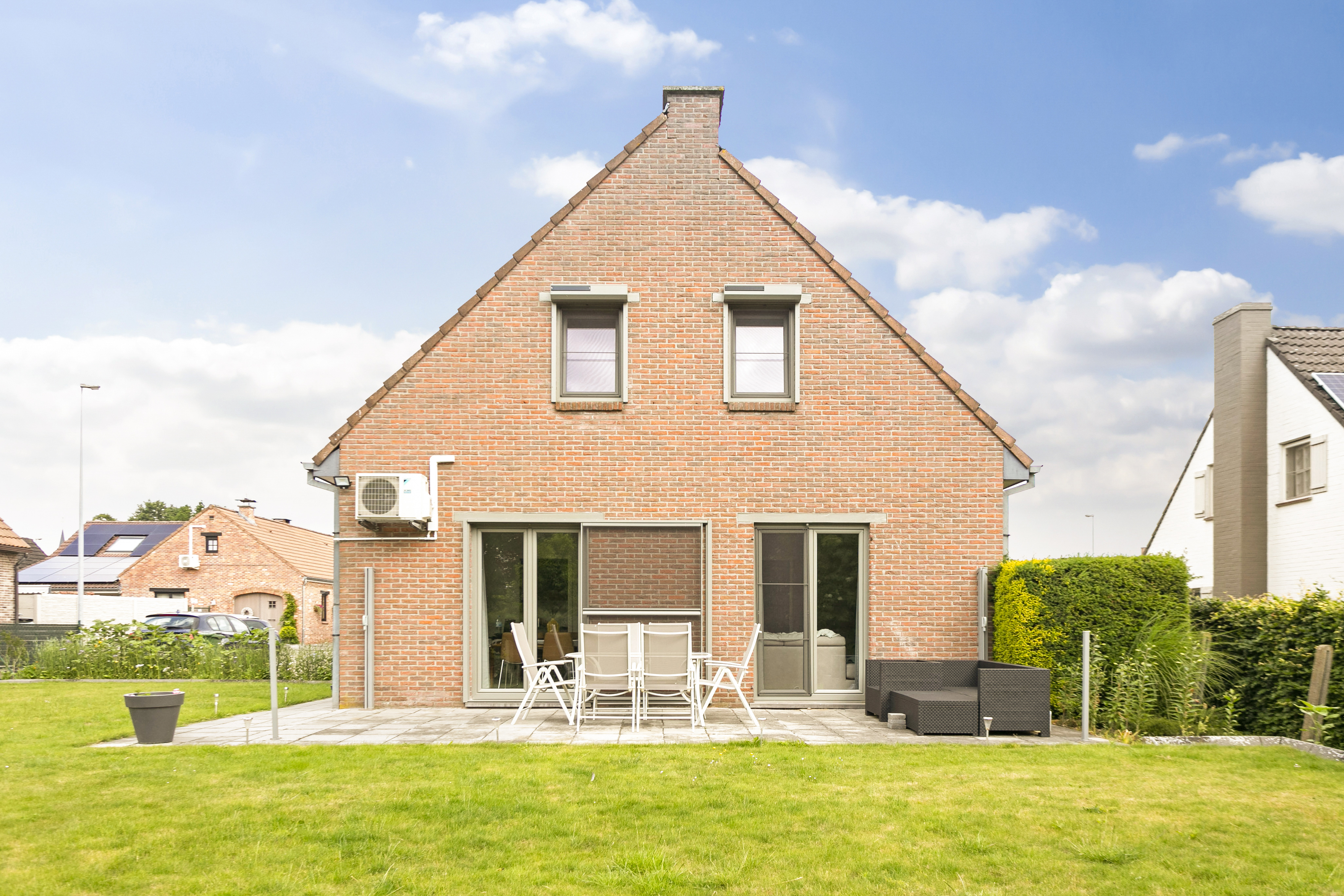 Achtergevel van een open bebouwing in baksteen met betongrijze dubbele en draai-kipramen, terrasdeuren en een schuifvliegenraam aan het gerenoveerde terras.