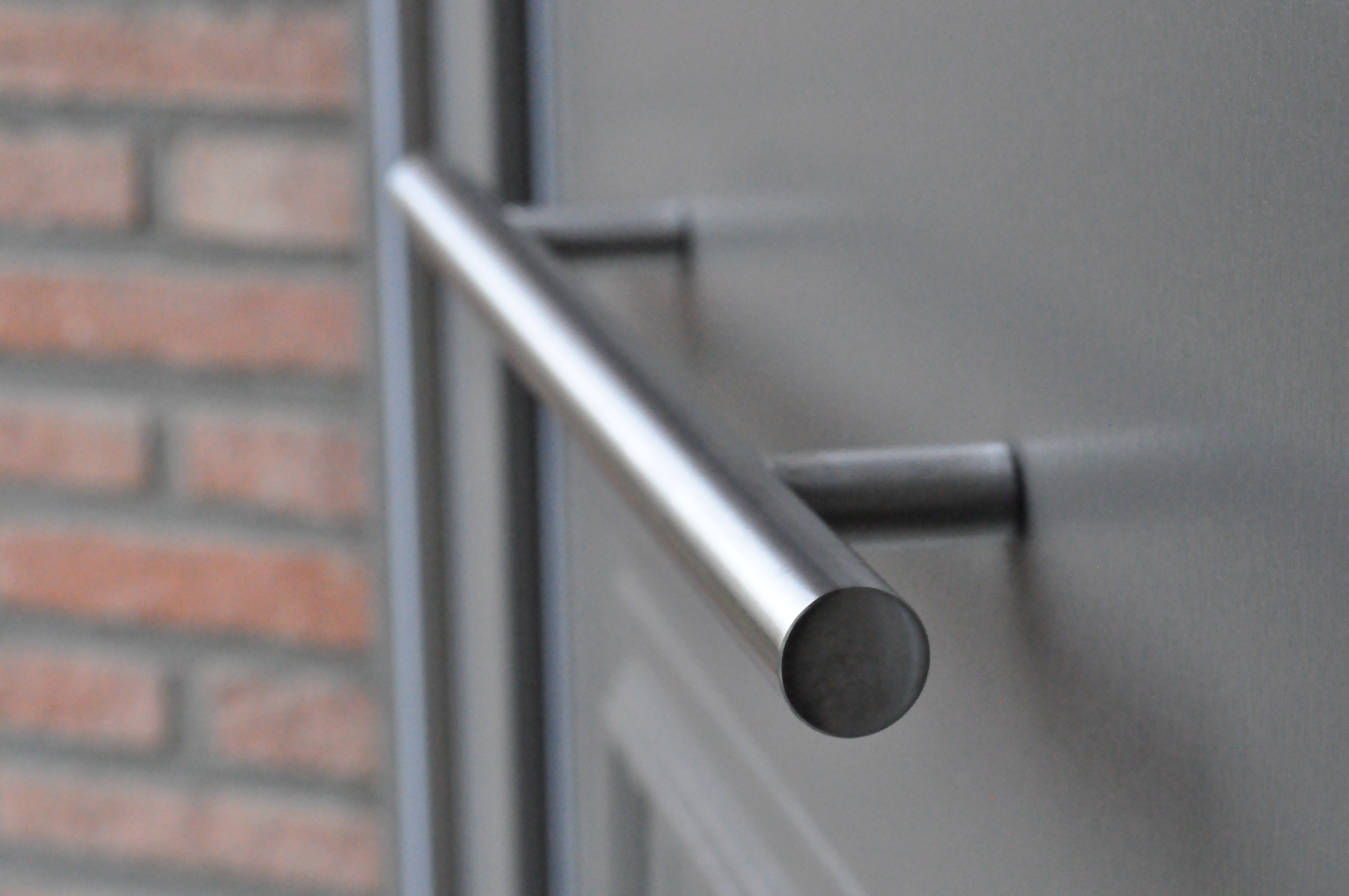 Detail van een donkergrijze deur met ronde metalen handgreep naast een bakstenen gevel en een smal zijlicht.