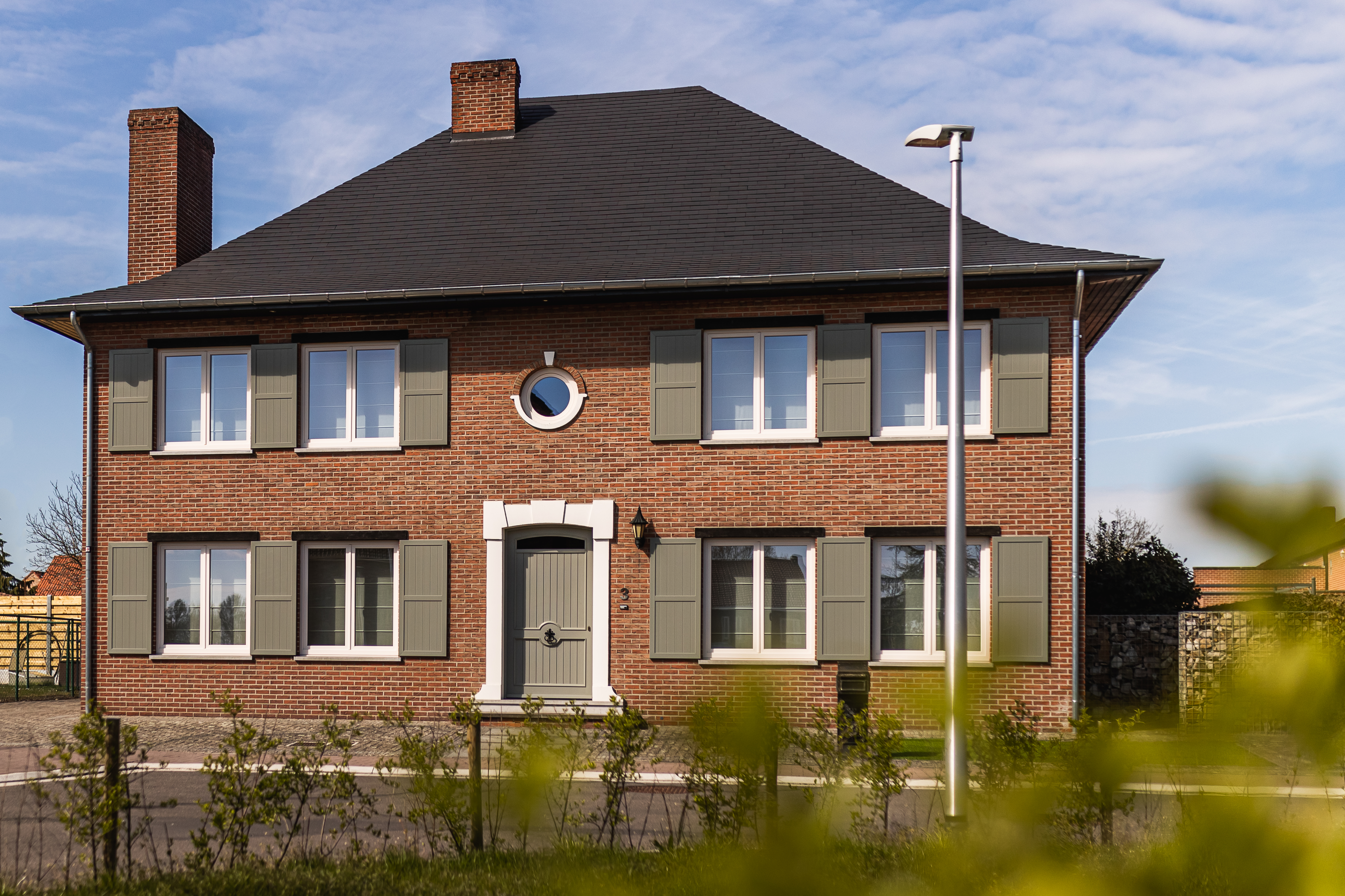 Gerenoveerde vrijstaande woning met crèmekleurige dubbele ramen en klapluiken in een gemoedelijke, tijdloze gevel van rode baksteen.