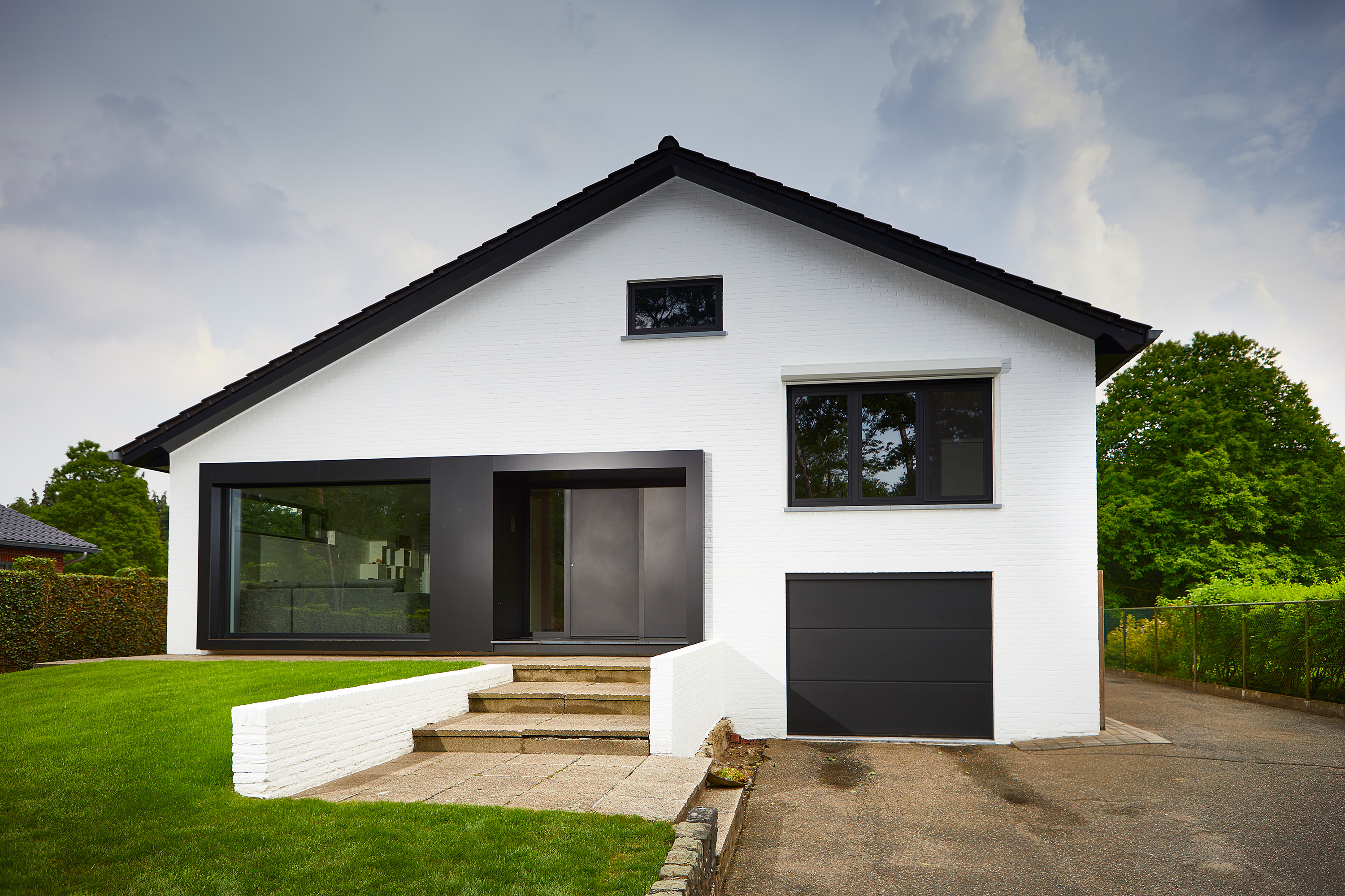 Gerenoveerde open bebouwing met witte gevel, zwarte SteelLook-ramen, grote glaspartijen, garage en trap naar de inkom.