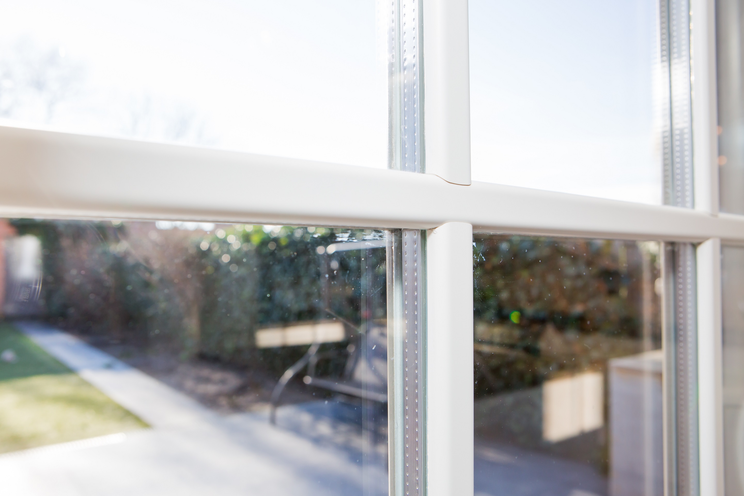 Klassiek wit raam met meerdere roedeverdelingen, met zicht op een tuin en een pad vanuit het lichte interieur.