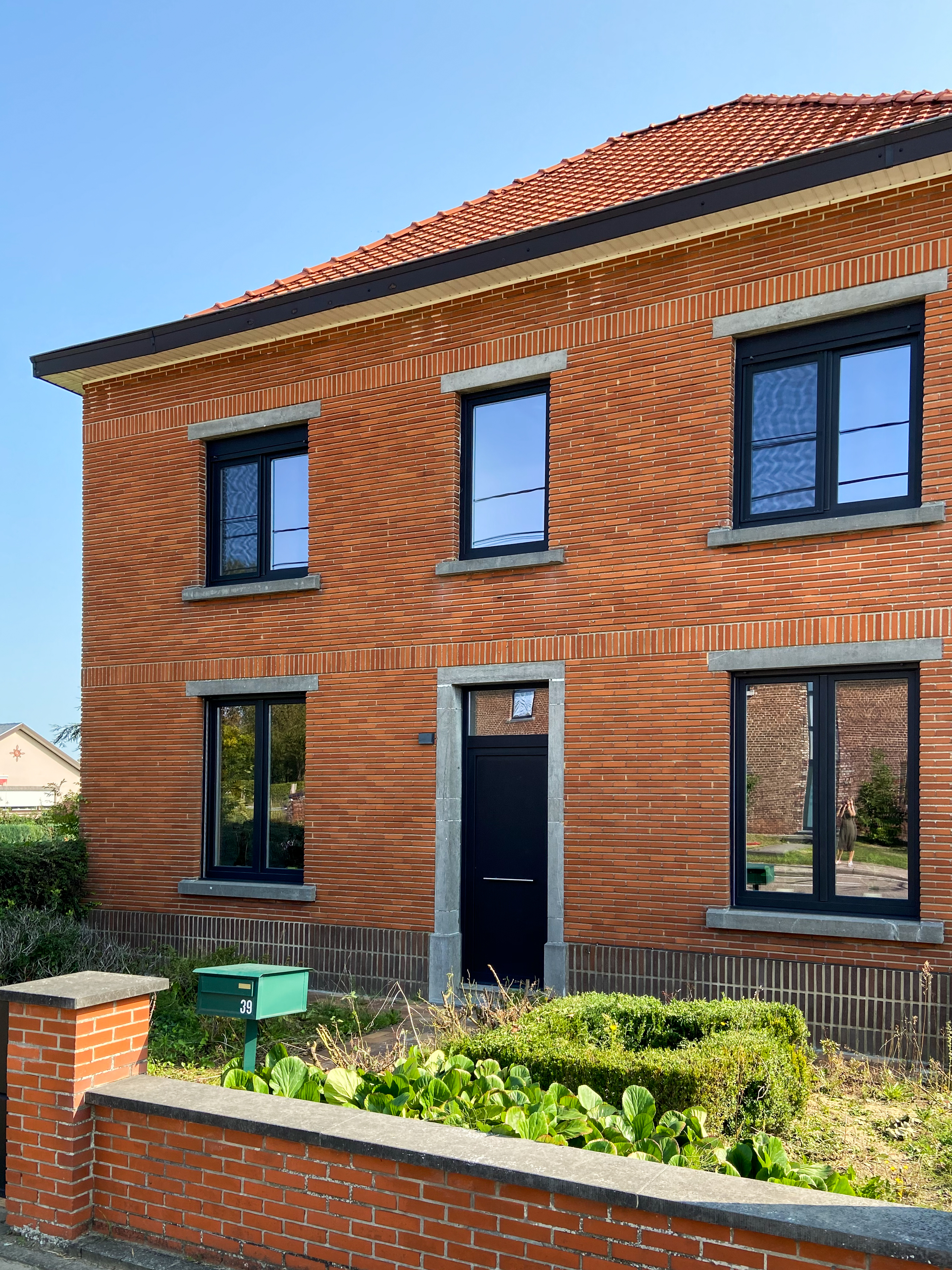 Gerenoveerde vrijstaande bakstenen woning met zwarte aluminium raamprofielen, dubbele en draai-kiepramen, en een donkere voordeur met bovenlicht.