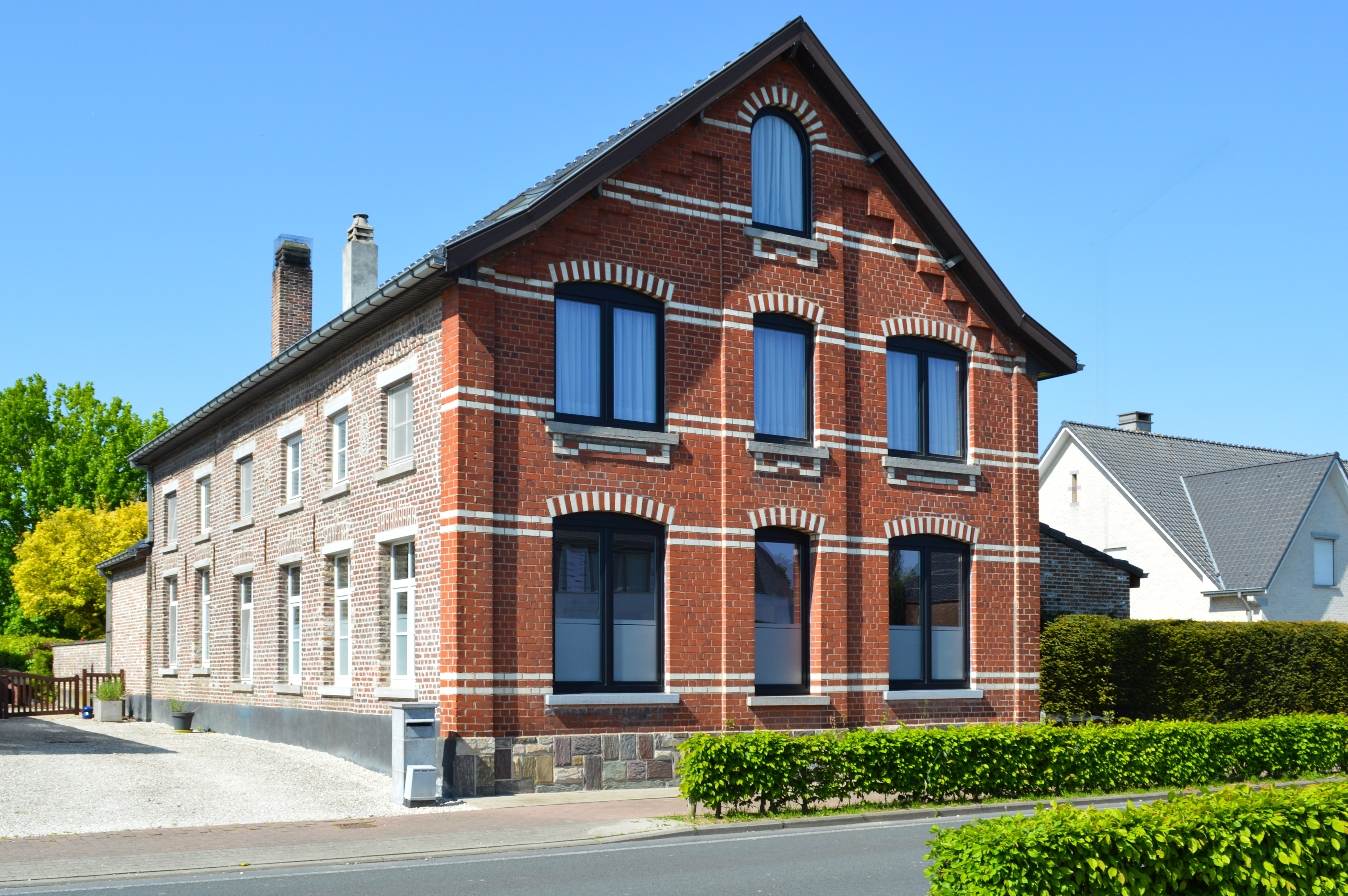 Bakstenen woning met matzwarte raamprofielen, dubbele ramen en draai-kipramen, aan de straatkant met een haag en voortuin.