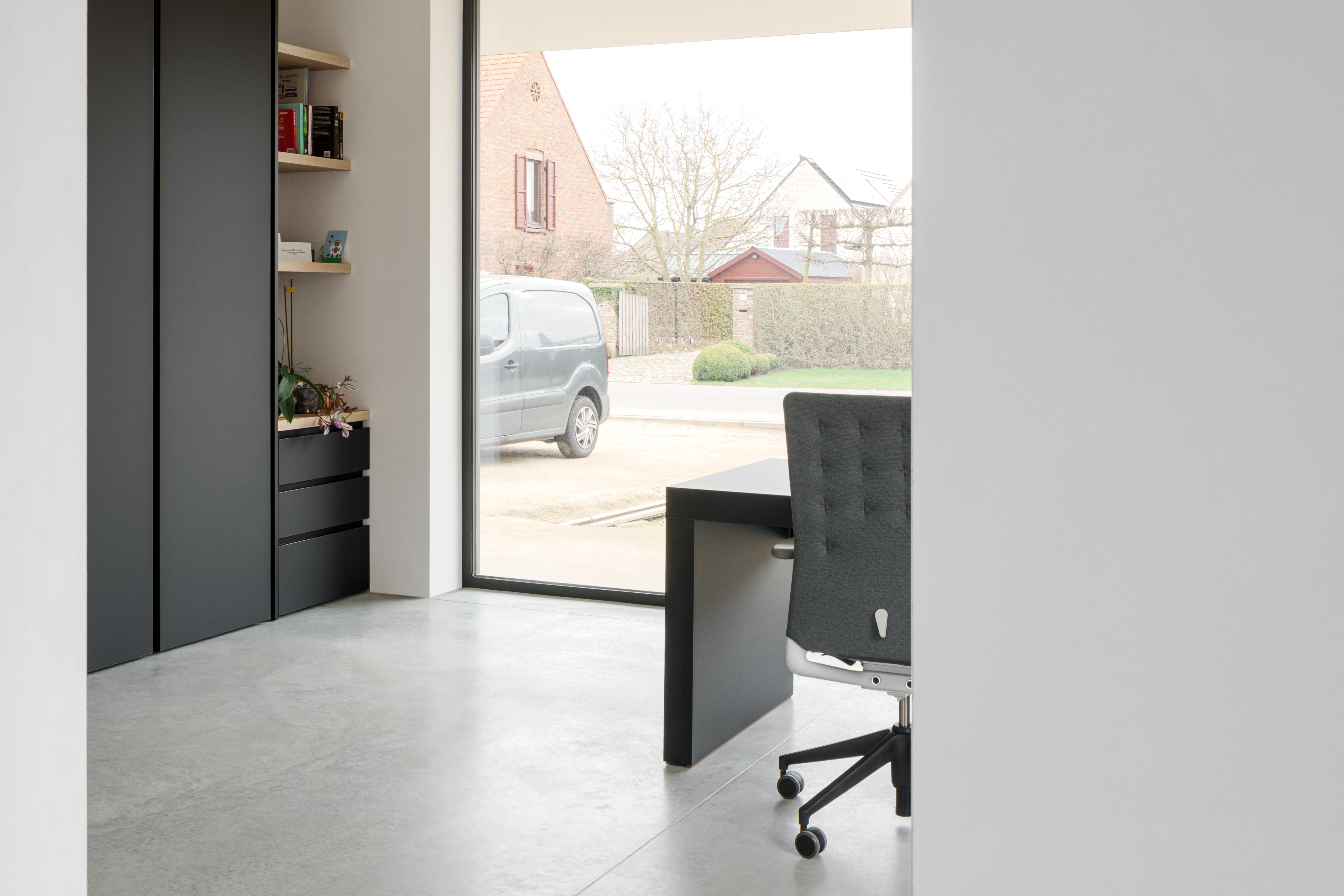 Modern vast raam met zwart raamprofiel in een stijlvol interieur, met zicht op de straat en omliggende woningen.